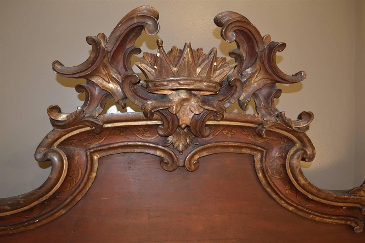 This exquisite bed was purchased in Europe and features superbly carved posts, foot rail and headboard with scrolls surrounding a center crown. The piece has a soft red poly-chrome finish with foliage and gilt accents. The original bed dates from