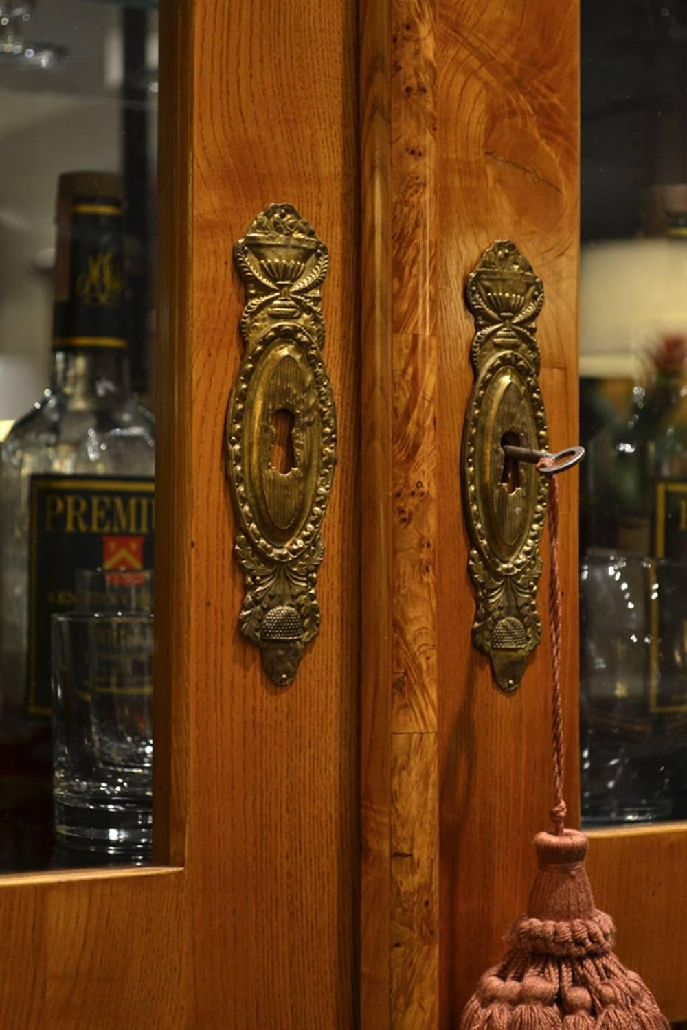 This mid-19th century cabinet has been made into a bar. The mirrored upper part holds glass shelves, and the decorative elm veneer is accented by ebonized details. It has had some minor repair to the veneer, but is otherwise in excellent condition.