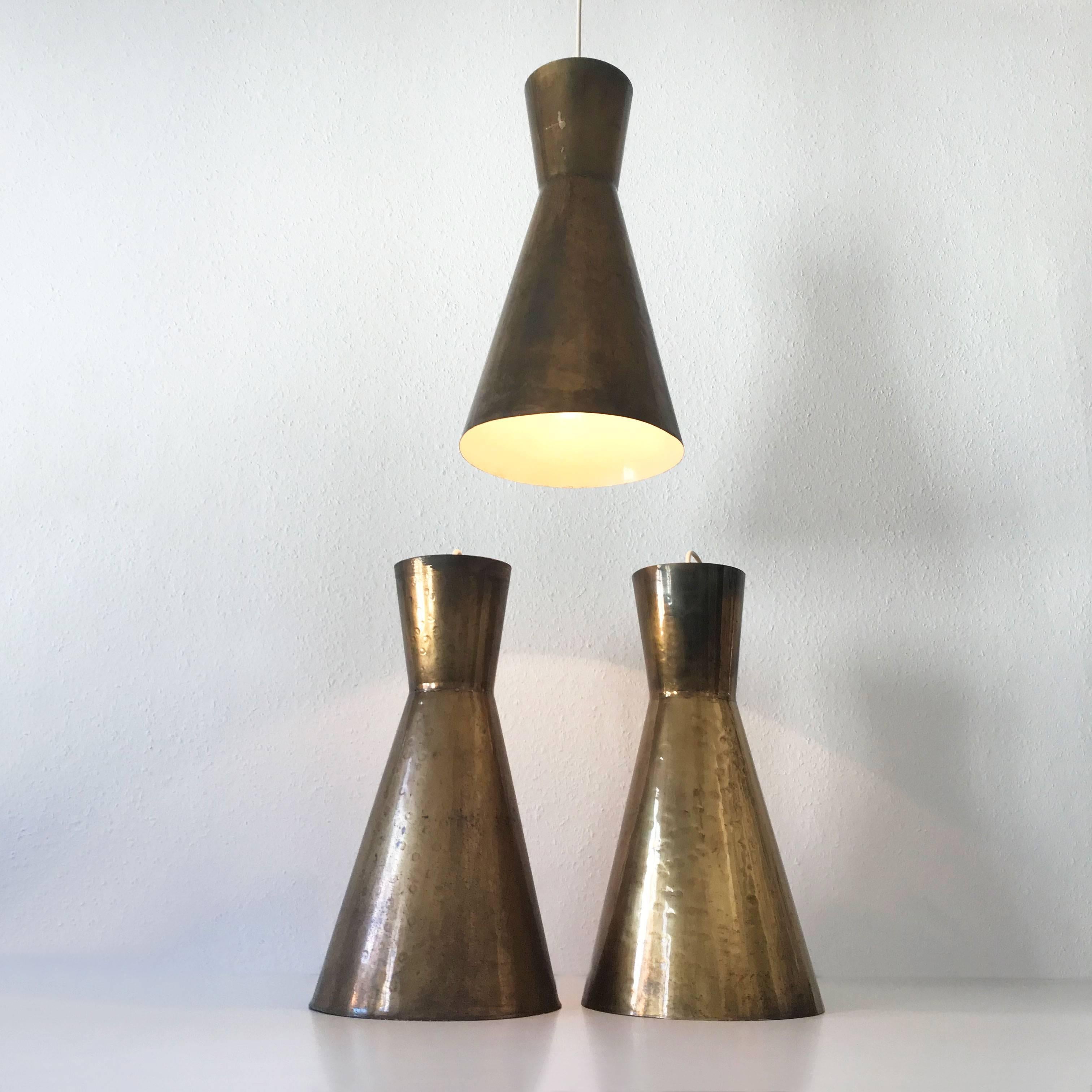 Set of three exceptional and large Mid Century Modern diabolo pendant lamps. Manufactured in Germany, 1950s.

Executed in hammered brass, each lamp needs 1 x E27 / E26 Edison screw fit bulb. They are wired, in working condition and run both on 110 /