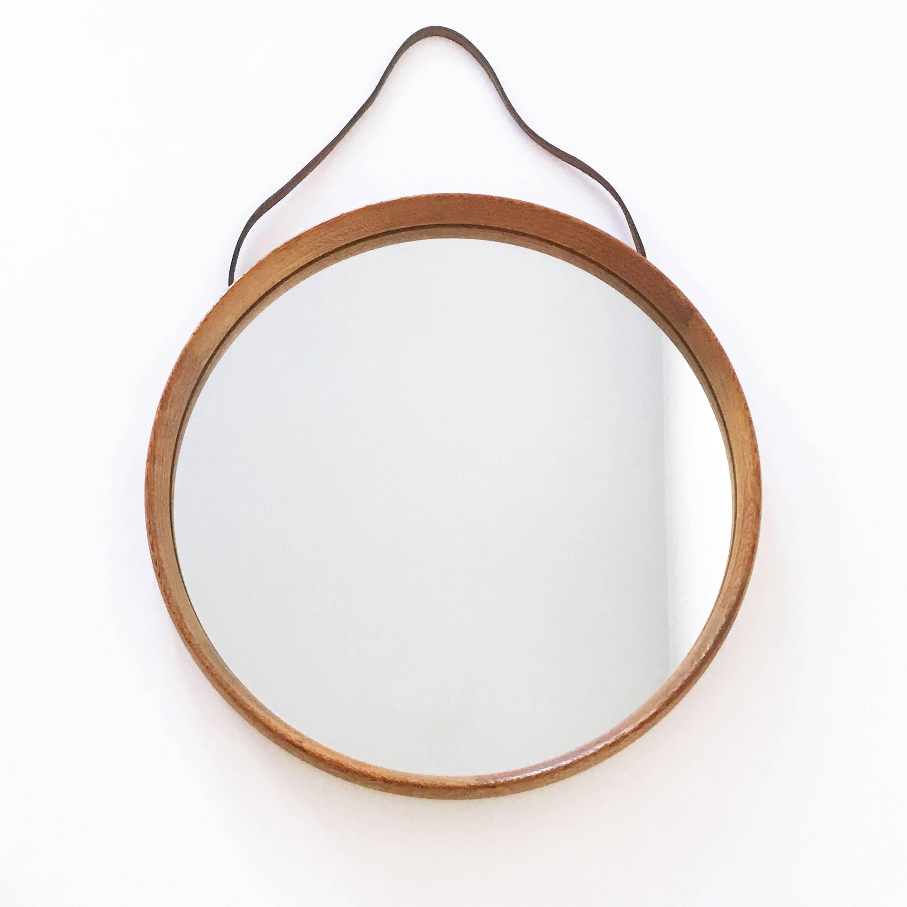 Elegant Mid Century Modern circular wall mirror with oakwood frame. Designed by Uno & Östen Kristiansson. Manufactured by Luxus, Vittsjö, Sweden, 1960s.

Executed in oak, mirror glass and leather.

Condition:
Good  original vintage condition. Wear