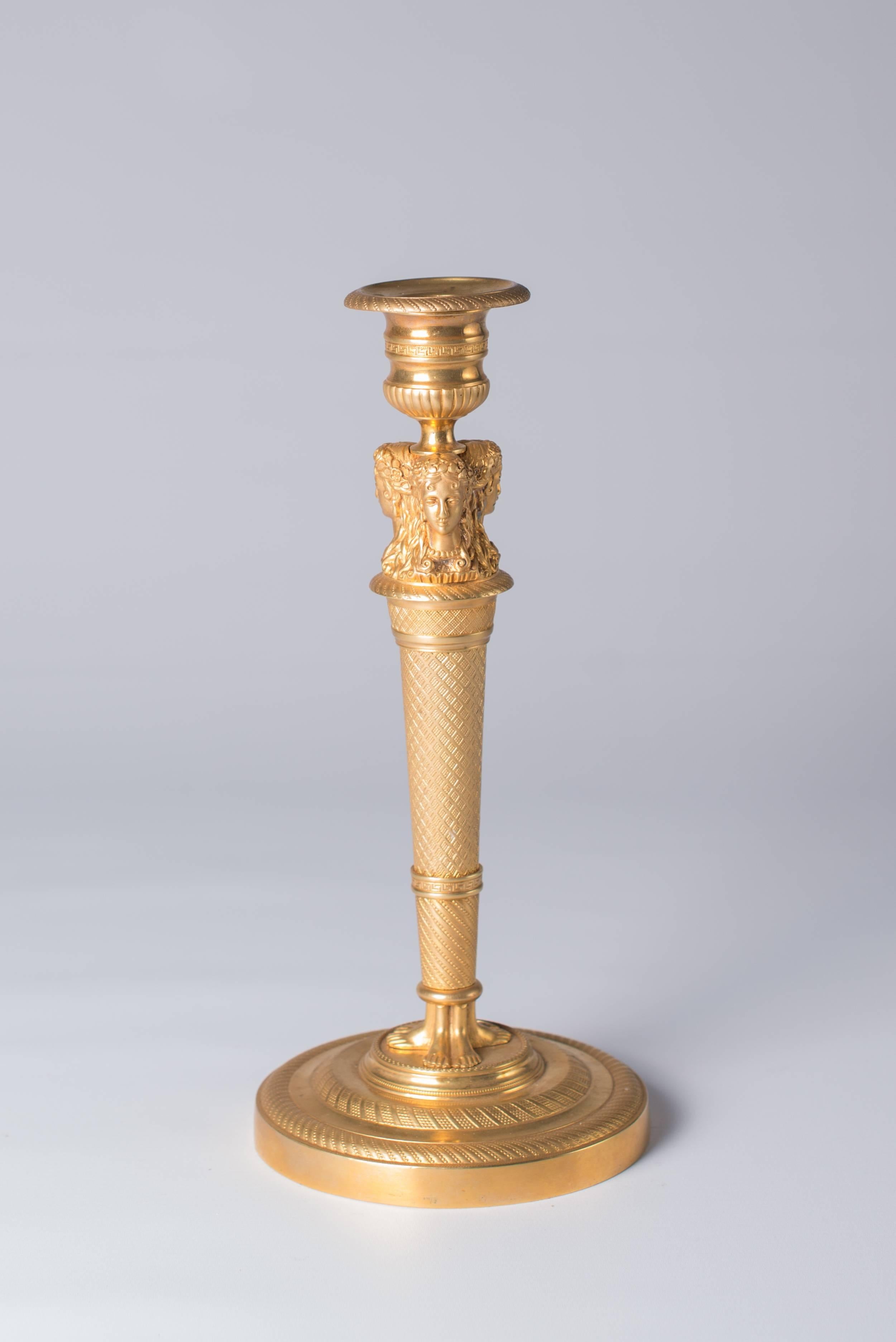 Pair of gilt bronze Empire candlesticks consists of circular low moulded base, the tapering stem with three caryatid feet below, three caryatid masks above and guilloche and stylized geometrical cast 'trellis' decoration between, vase-shaped