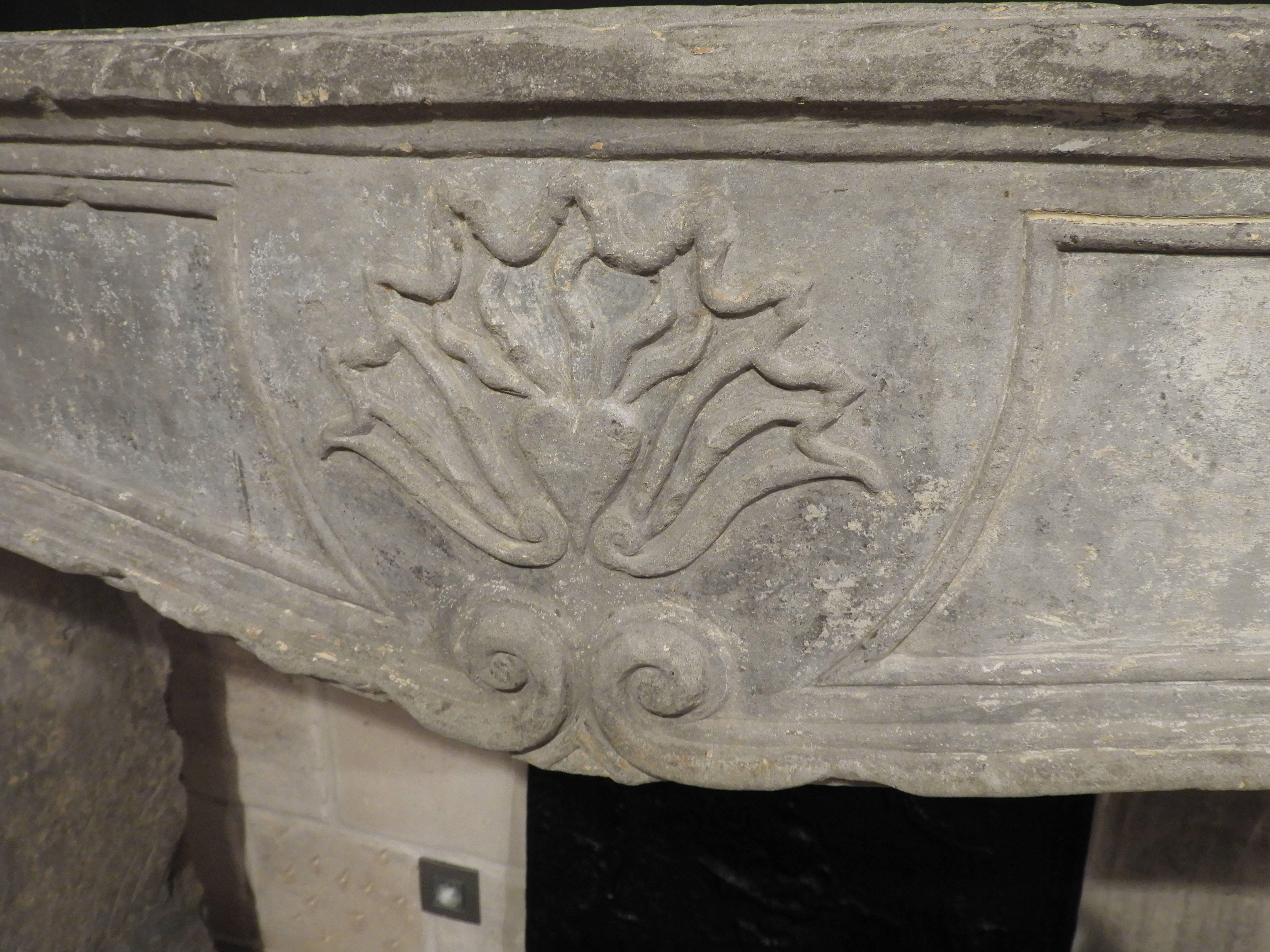 18th century limestone fireplace in grey French limestone. The fireplace is warn, rustic and probably comes out of a presbytery. The center of the fireplace is the sacred heart: symbol of the long-suffering love and compassion of the heart of Christ