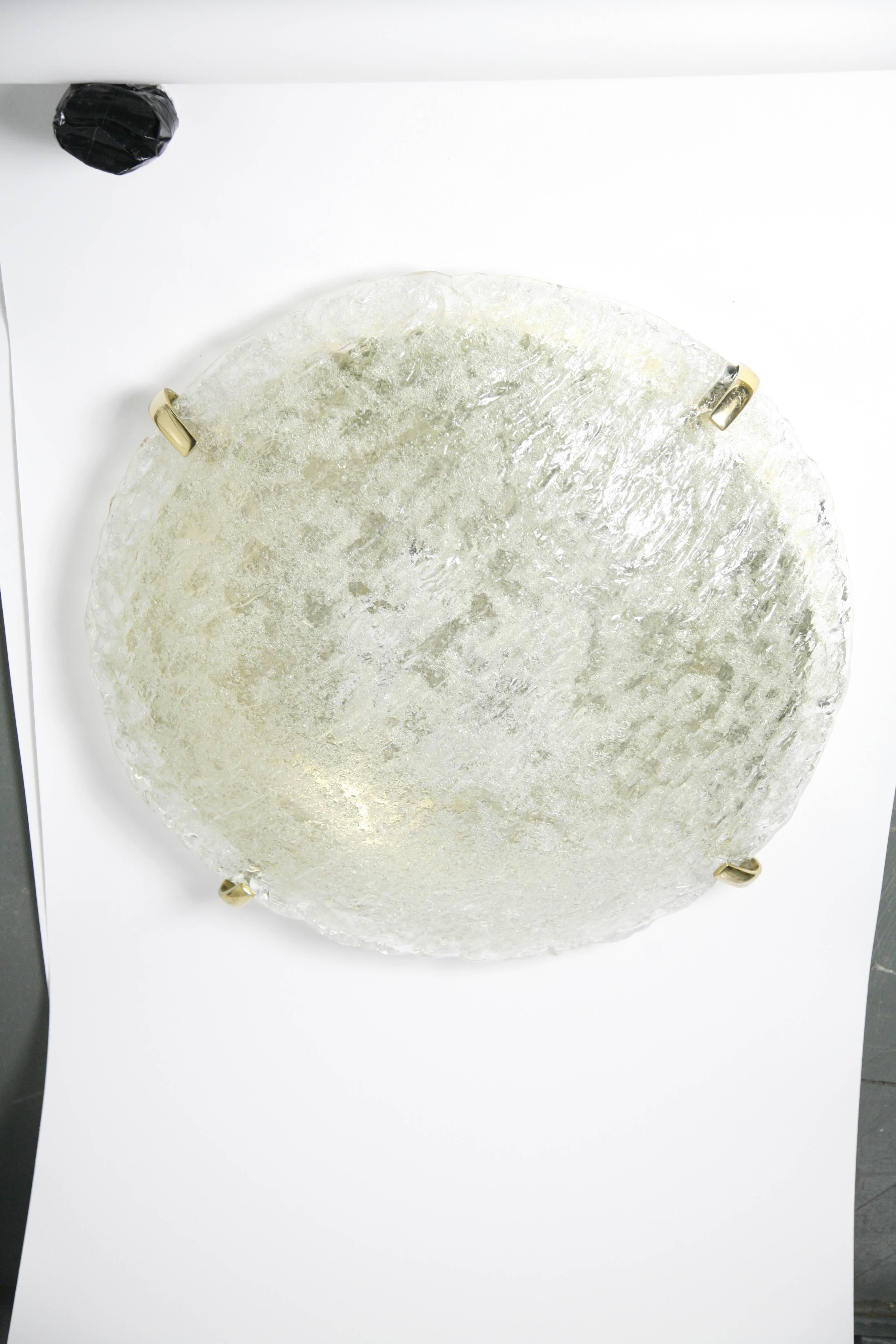 Flush mount by Kaiser, Germany, 1980 a round clear glass diffuser dome shaped thick and heavy glass that is smooth on the outside and matte on the inside four brass finials, eight European sockets on a brass frame.
On the inside of the glass is in