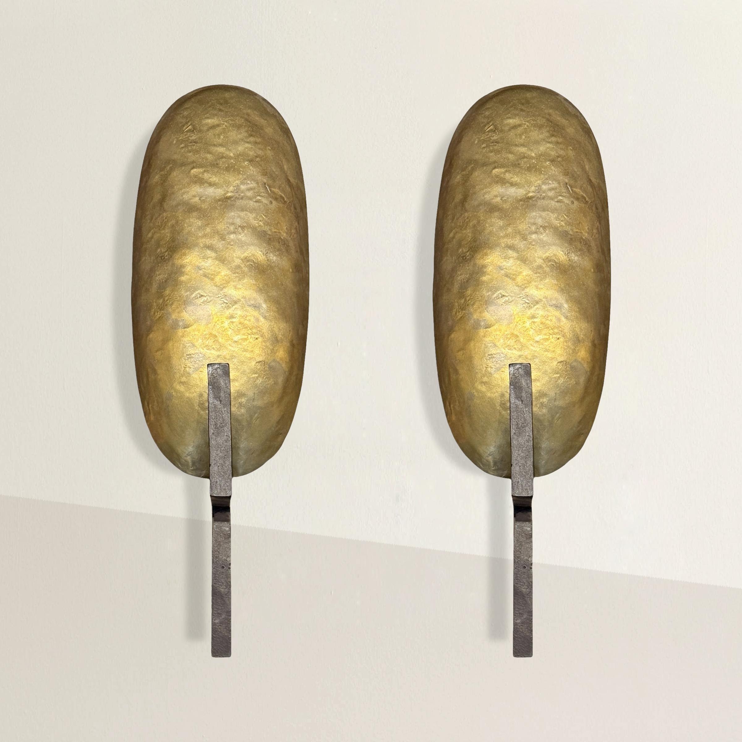 A study in restrained elegance, this pair of sconces was crafted by Paul Ferrante in Los Angeles, a studio renowned for its commitment to timeless design and impeccable craftsmanship. Each sconce features a hand-wrought iron frame supporting a