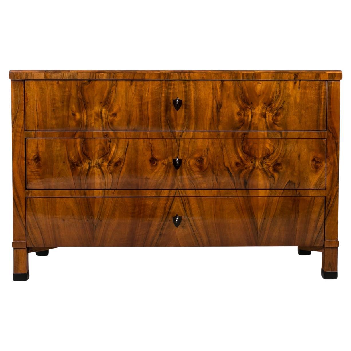 This Biedermeier chest of drawers was made in the 19th Century, originating from Germany. Crafted with precision and attention to details, construction made of pine wood adorned with exceptional walnut veneer. Admire its distinguished features,