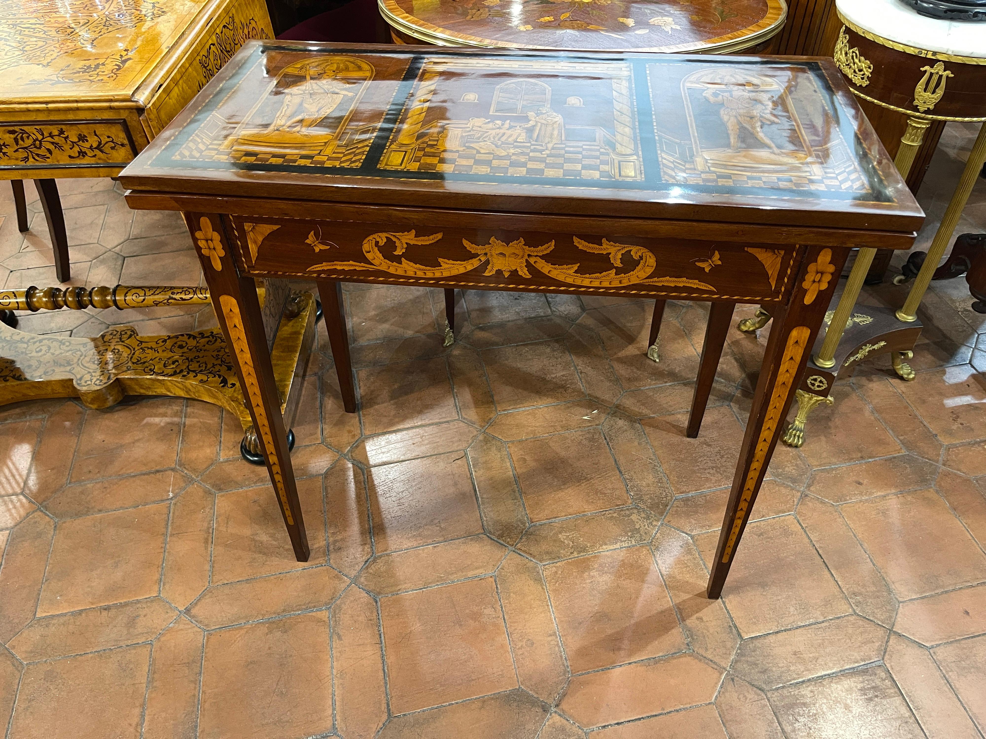 Dutch game table, Louis XVI era, mahogany and walnut wood, finely inlaid.
We are faced with a work of high cabinet-making, inlaid on all sides in woods of fruit on the plan is depicted in the figure of an alchemist taken in the making of a potion