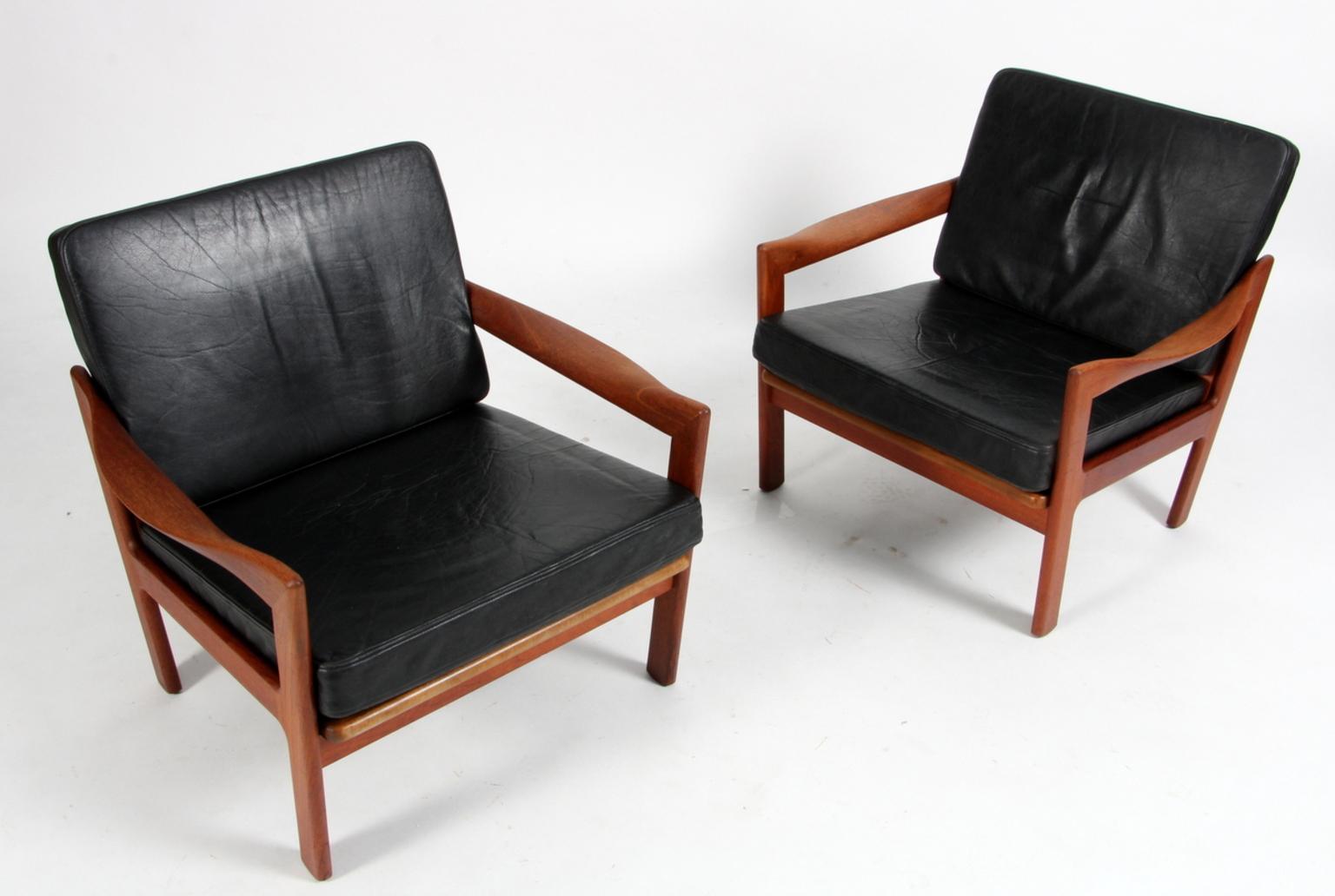 A pair of Illum Wikkelso for N. Eilersen lounge chairs in solid teak with impressive armrest.

Original upholstered with black leather.

Model 20, made by N. Eilersen.

Impressive craftmanship with the most beautiful curved armrests.