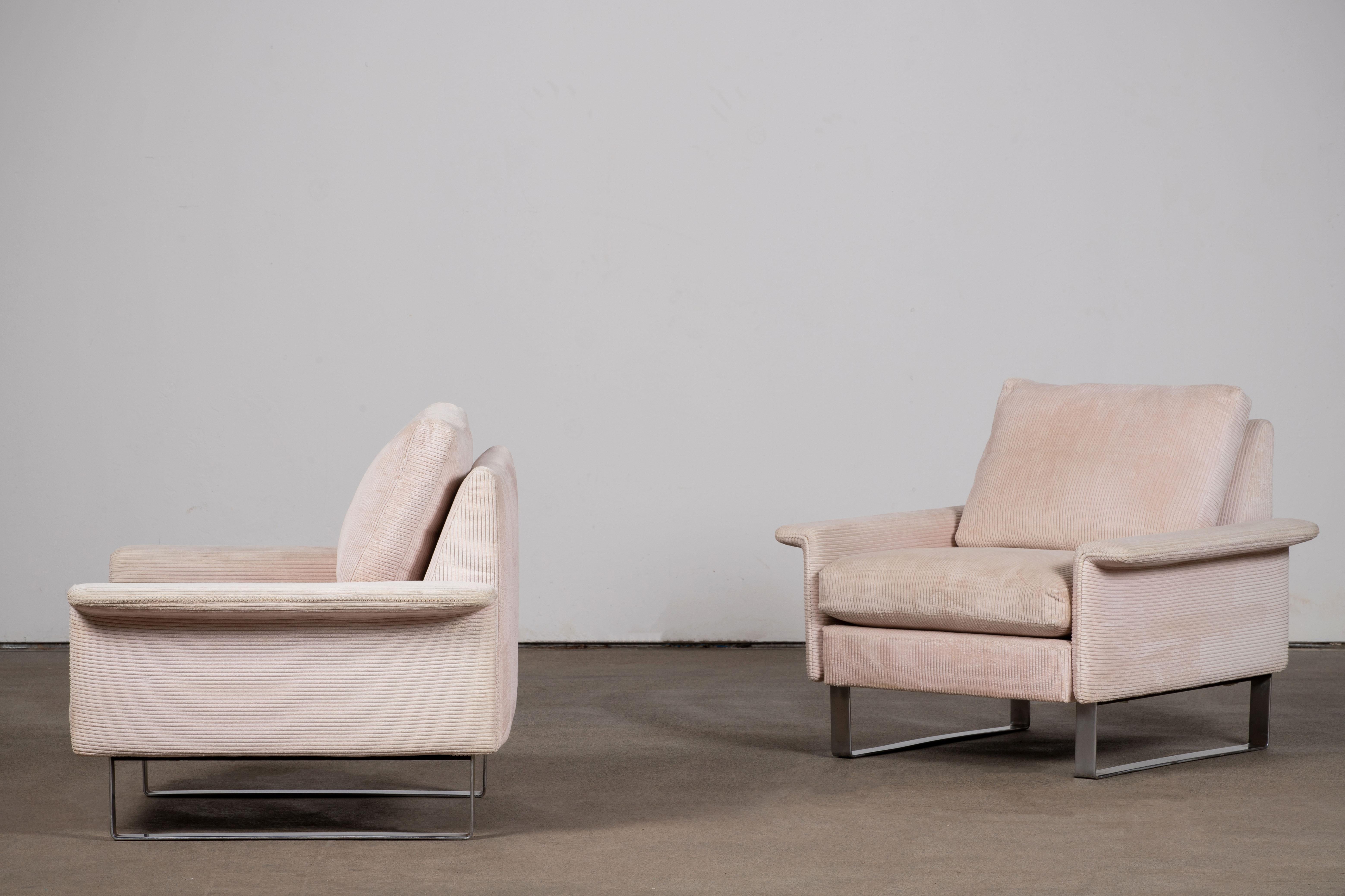 Esta pareja de sillones de salón, una composición de tranquila monumentalidad ejecutada a la manera de Milo Baughman, revela un vocabulario de claridad geométrica y aplomo escultórico. Cada silla se presenta como un cubo tapizado, aparentemente