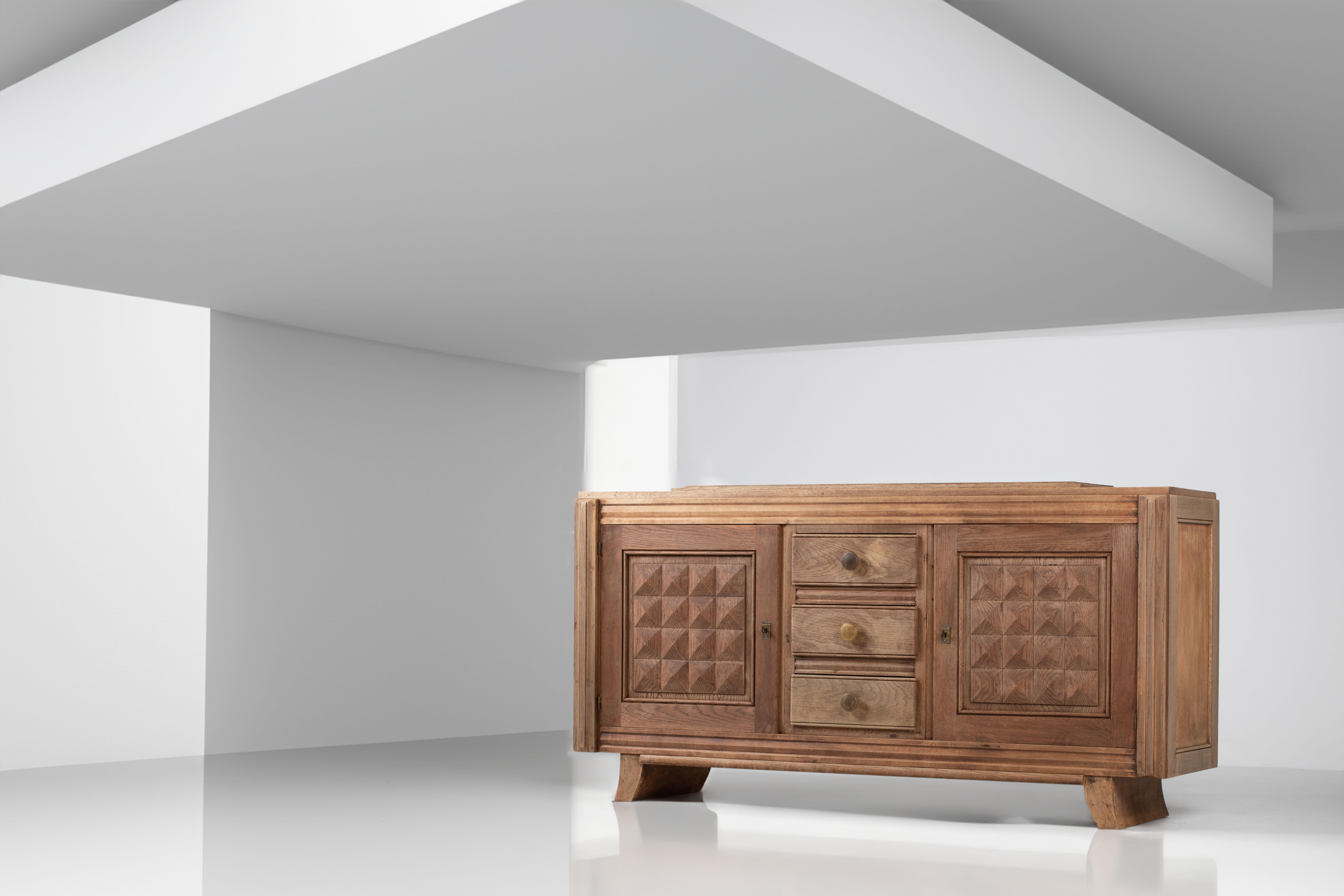 Composizione dalla simmetria risoluta e dalla tranquilla monumentalità, questa credenza francese degli anni '40 in rovere massiccio incarna lo spirito della visione di Charles Dudouyt: un linguaggio di sobrietà scultorea e cadenza