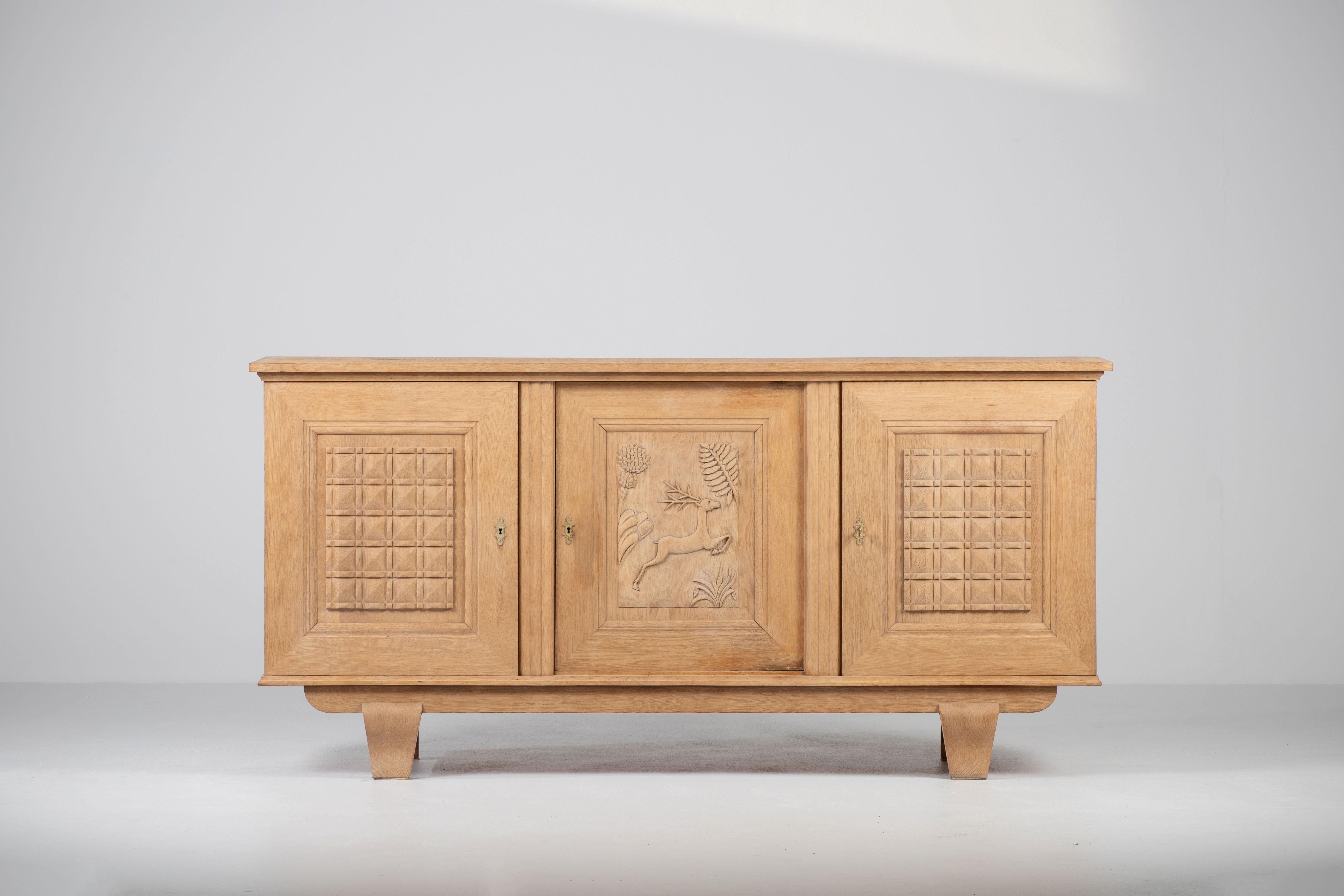 A composition of stoic monumentality, this French sideboard, circa 1940, articulates a language of sculptural reserve and regional narrative. Framed within a broad rectilinear carcass, the façade unfurls as a triptych of carved panels—its central