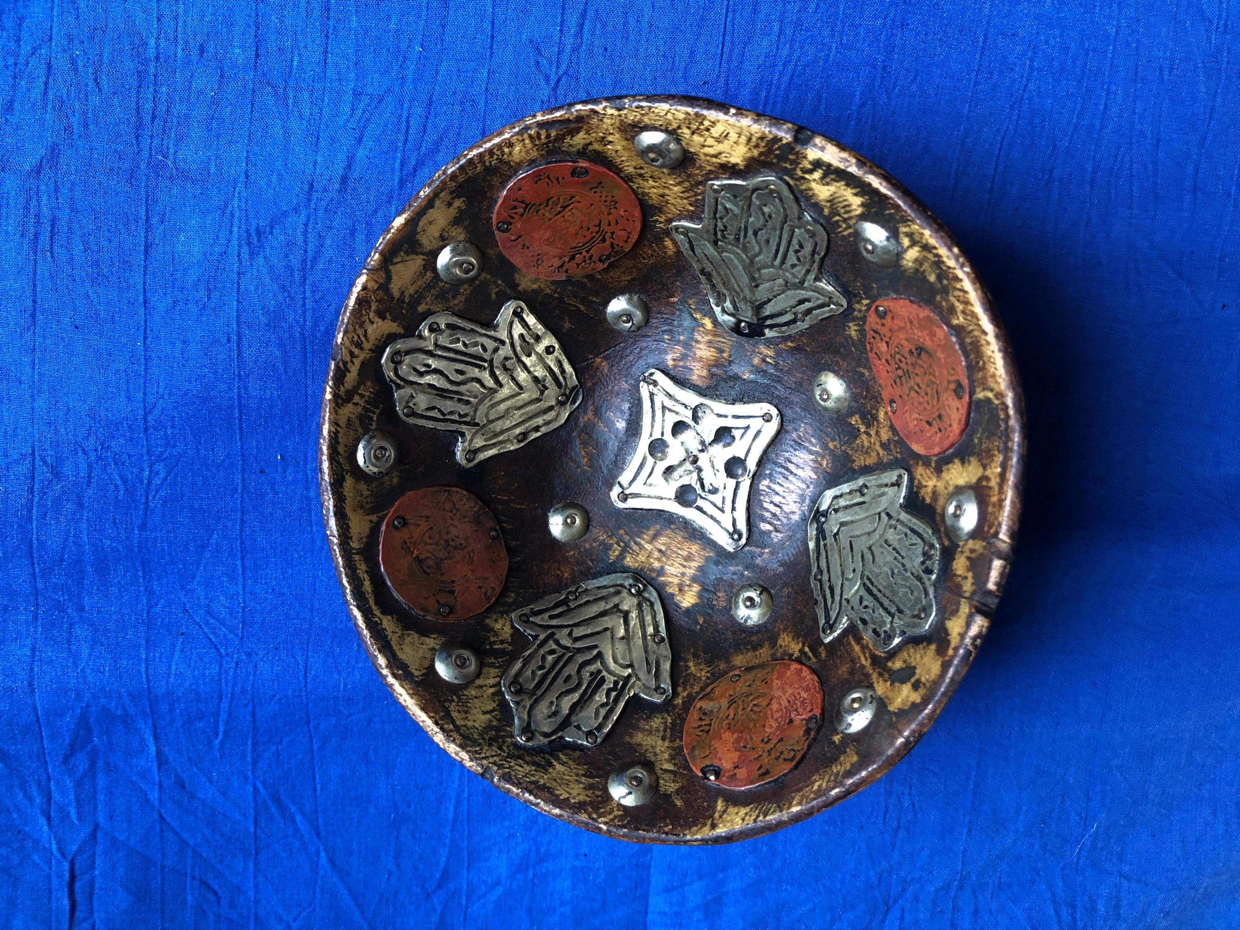 Crafted from a single piece of thick hardwood, this hand-carved bowl is decorated with antique silver Rial coins dating back to 1913. The coins have been hammered and are stained with henna, giving them a ruddy glow. Hand-forged chased Hamsa (Hand