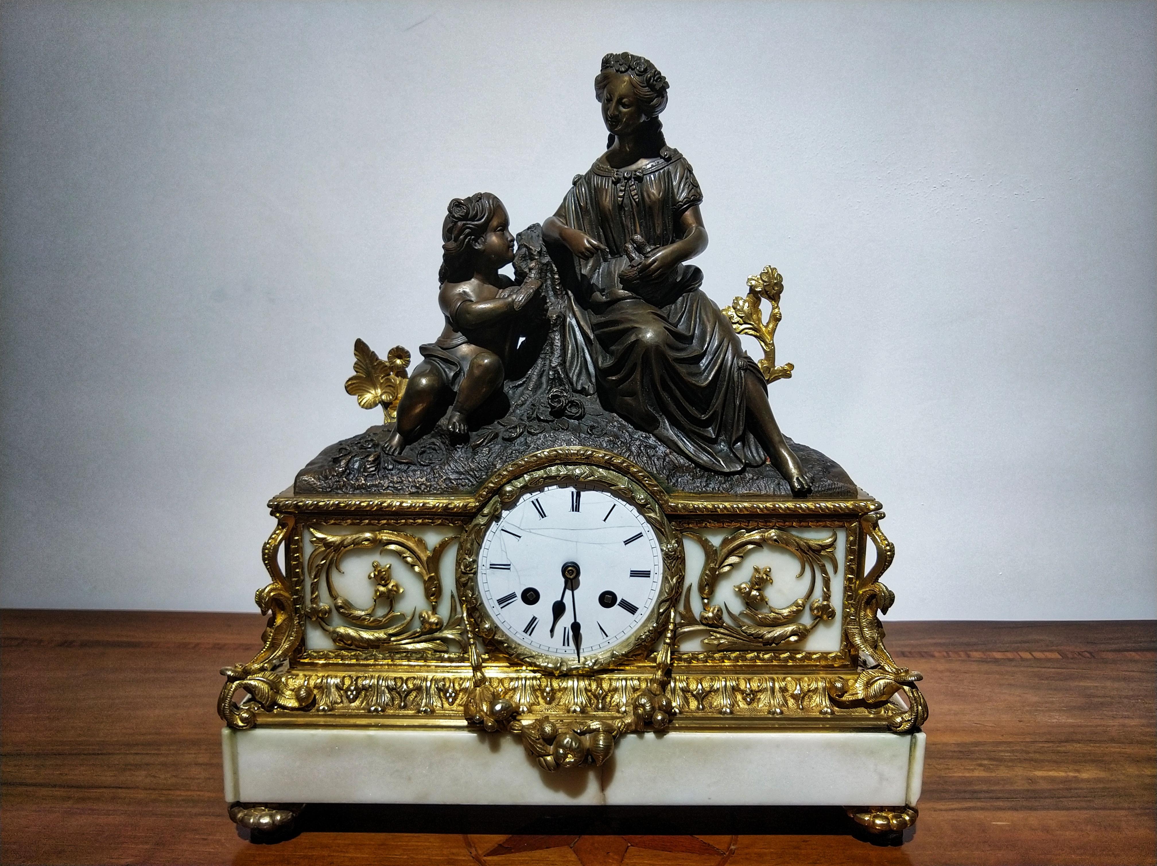 Elegant Napoleon III mantel clock by Japy Freres & Cie with a woman and a child leaning on a log, saving a bird's nest. The central part is full of floral motifs of gilded bronze with white marble as a background, the dial is ceramic and at the