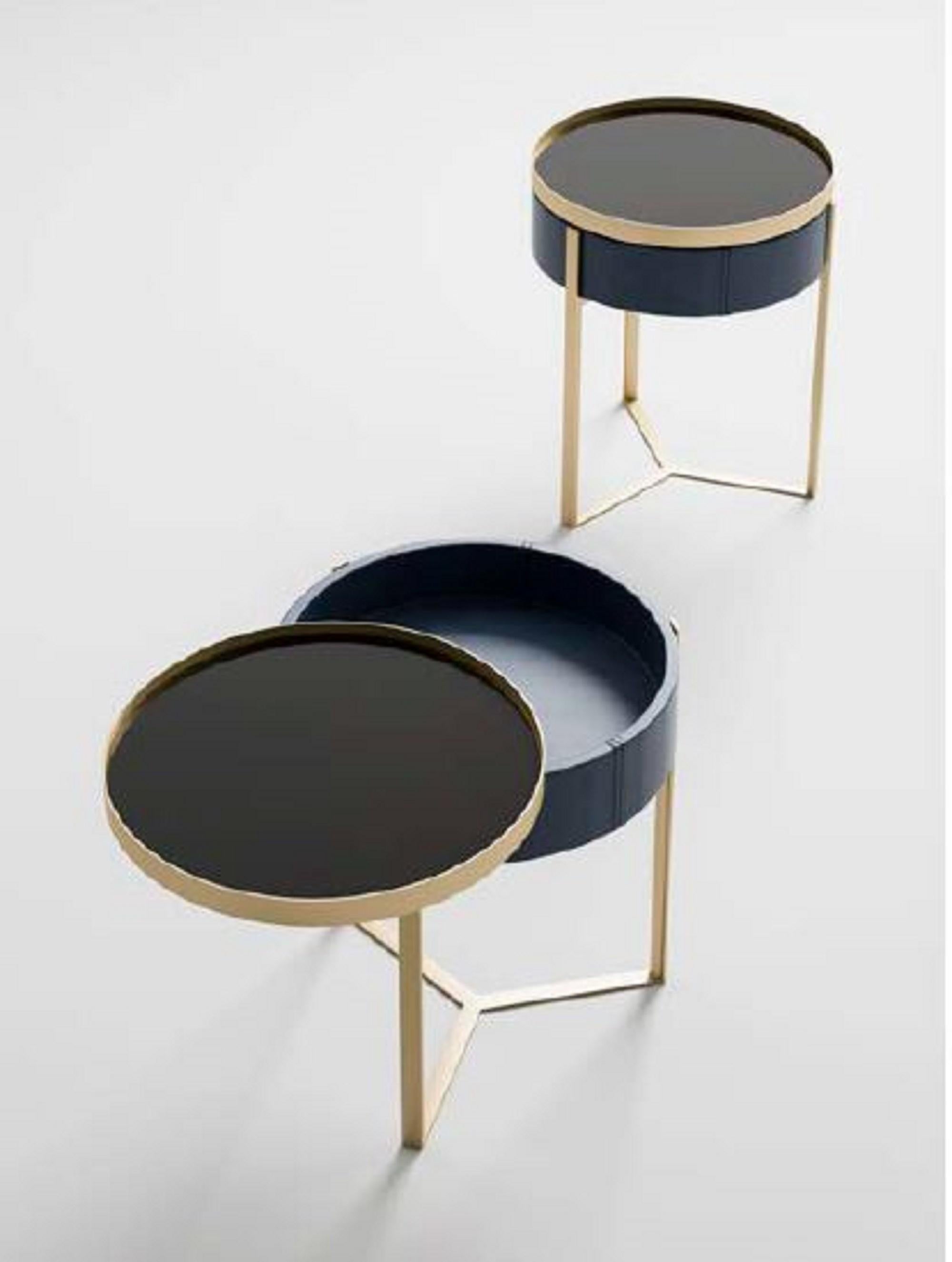 The Must Have round nightstand by Malerba is an elegant and functional piece of furniture. It features a round shape, a metal frame, leather upholstery, and a rotating glass top with a metal frame. Its pure and embracing lines are enriched with