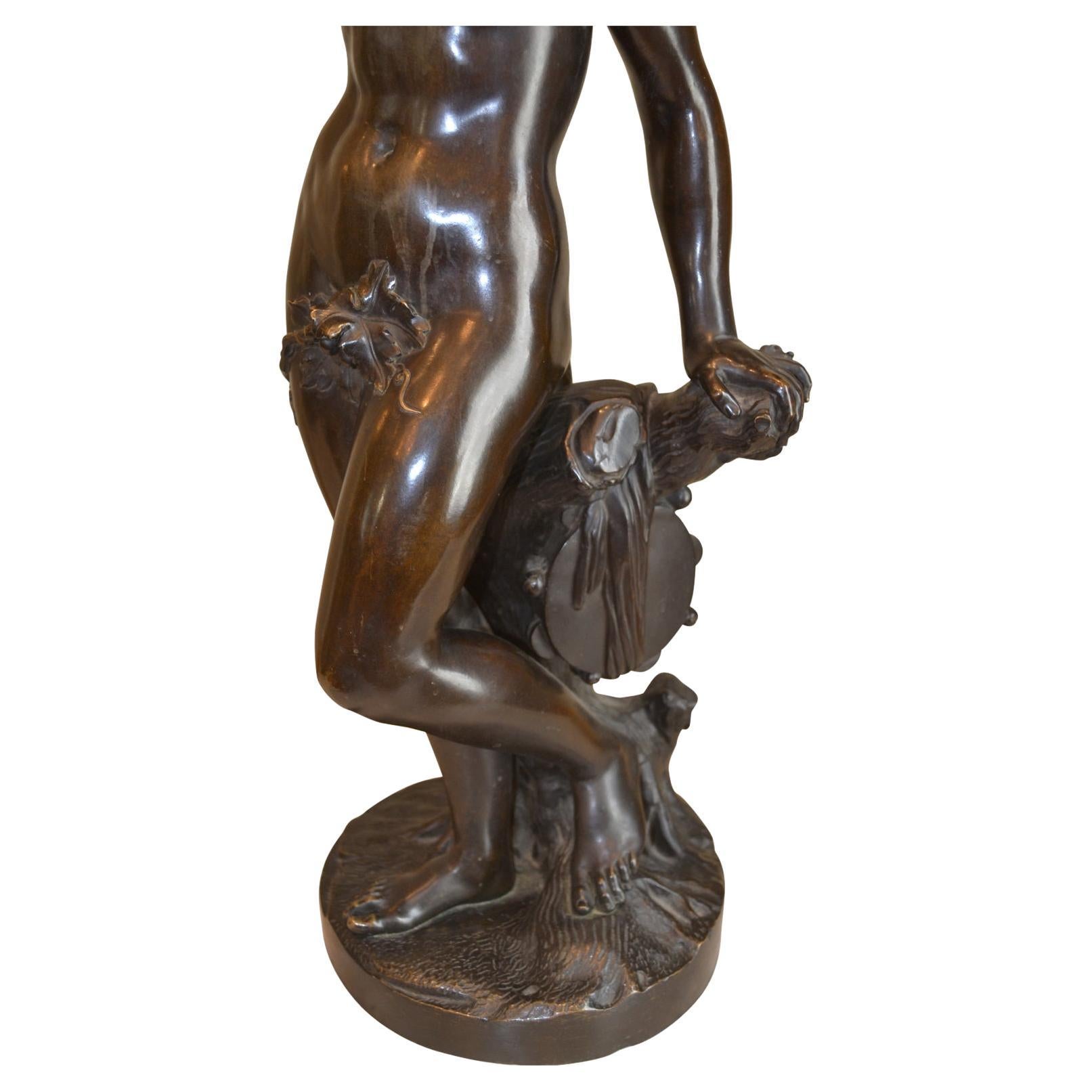 A patinated bronze allegorical statue of a nude bacchante, the roman goddess of wine, in the manner of Clodion with right hand raised and holding a bunch of grapes, while the other rests on a trunk of an ancient vine. Likely cast by one of the major