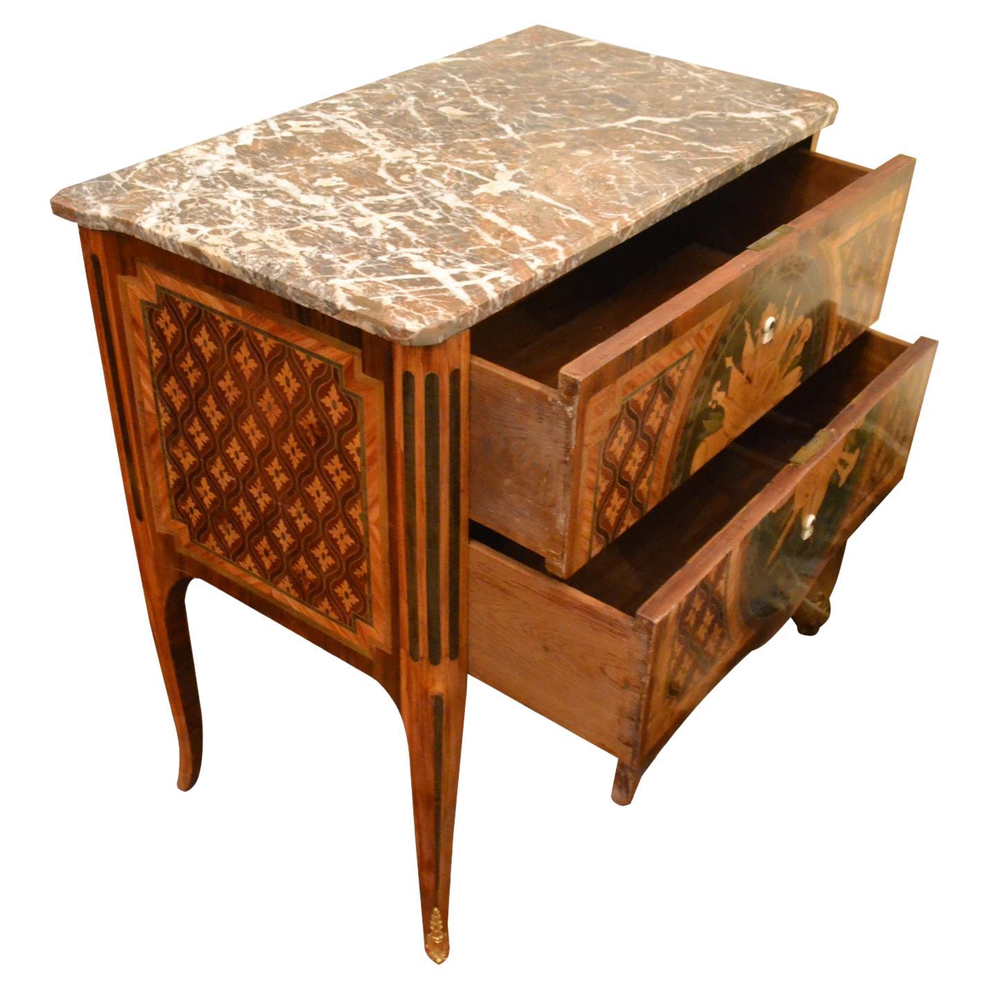 A period 18th century French two drawer chest with a breche marble top, the oak carcass veneered in various exotic woods in an overall geometric design. The large inlaid oval panel to the front shows various musical instruments in a heraldic