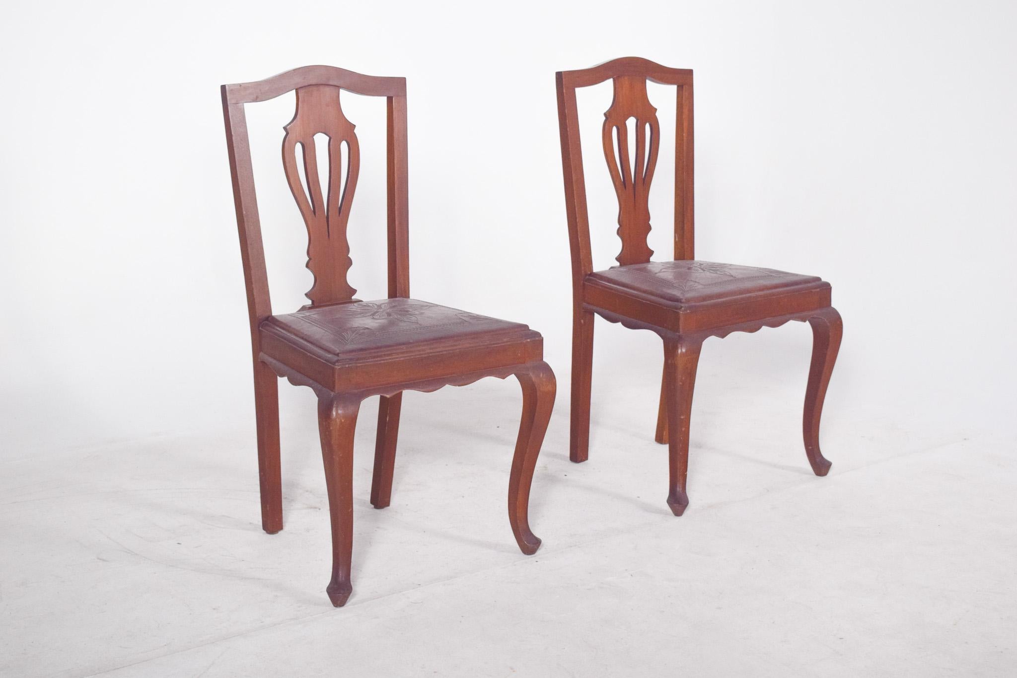 Paire de chaises avec assise en cuir gaufré. Avec un design inspiré du style Queen Anne, ils présentent des lignes élégantes et courbes, ainsi que des détails sculptés sur le dossier en forme de goutte stylisée, typique du XVIIIe siècle. Les pieds