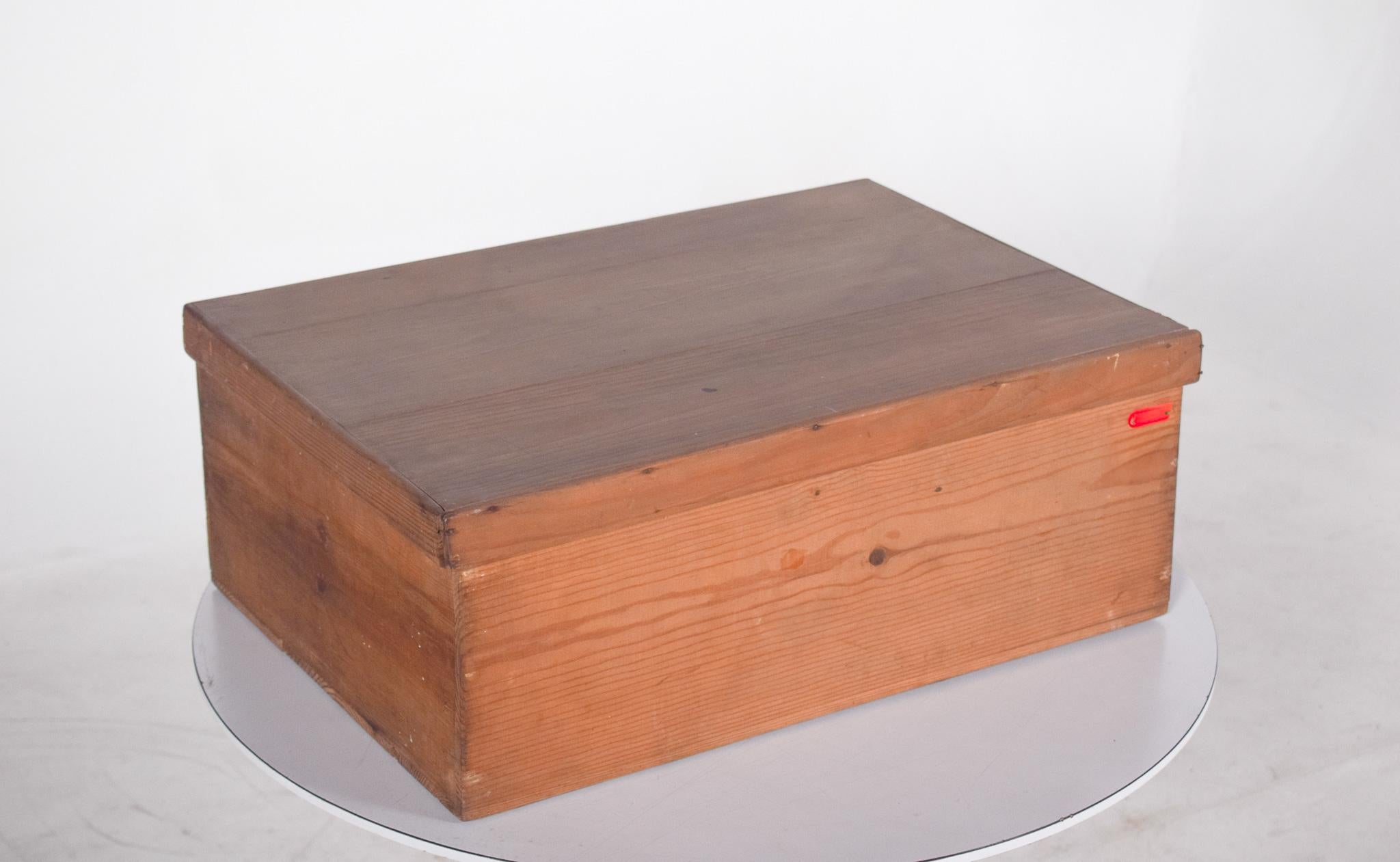 Scatola rettangolare in legno. Con coperchio ad apertura verticale, realizzato con assi di legno naturale non verniciato o non verniciato. Le facce esterne mostrano i segni naturali del materiale, come venature e nodi, conferendo un aspetto rustico.