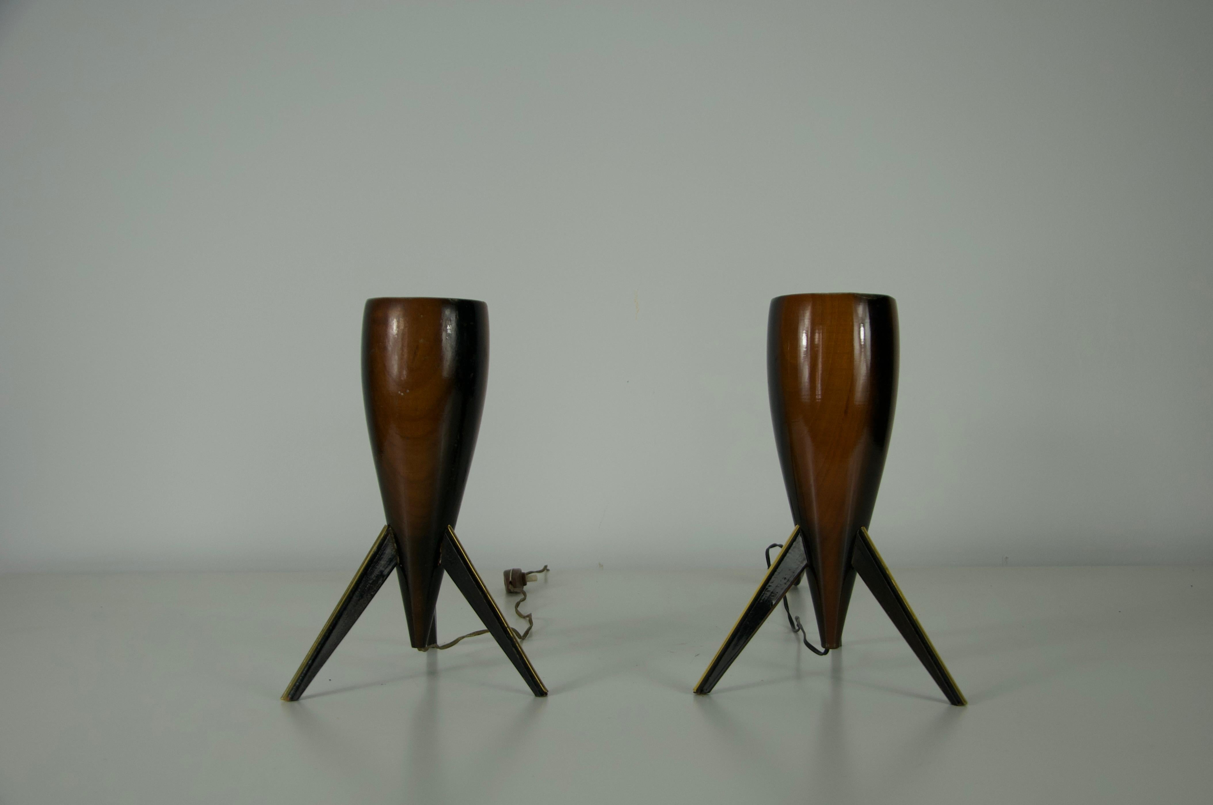 Cette paire sculpturale de lampes de table italiennes des années 1970 présente un design moderne du milieu du siècle. Chaque lampe présente un corps en bois élancé et allongé, avec une finition riche et chaude, reposant sur des pieds en forme de