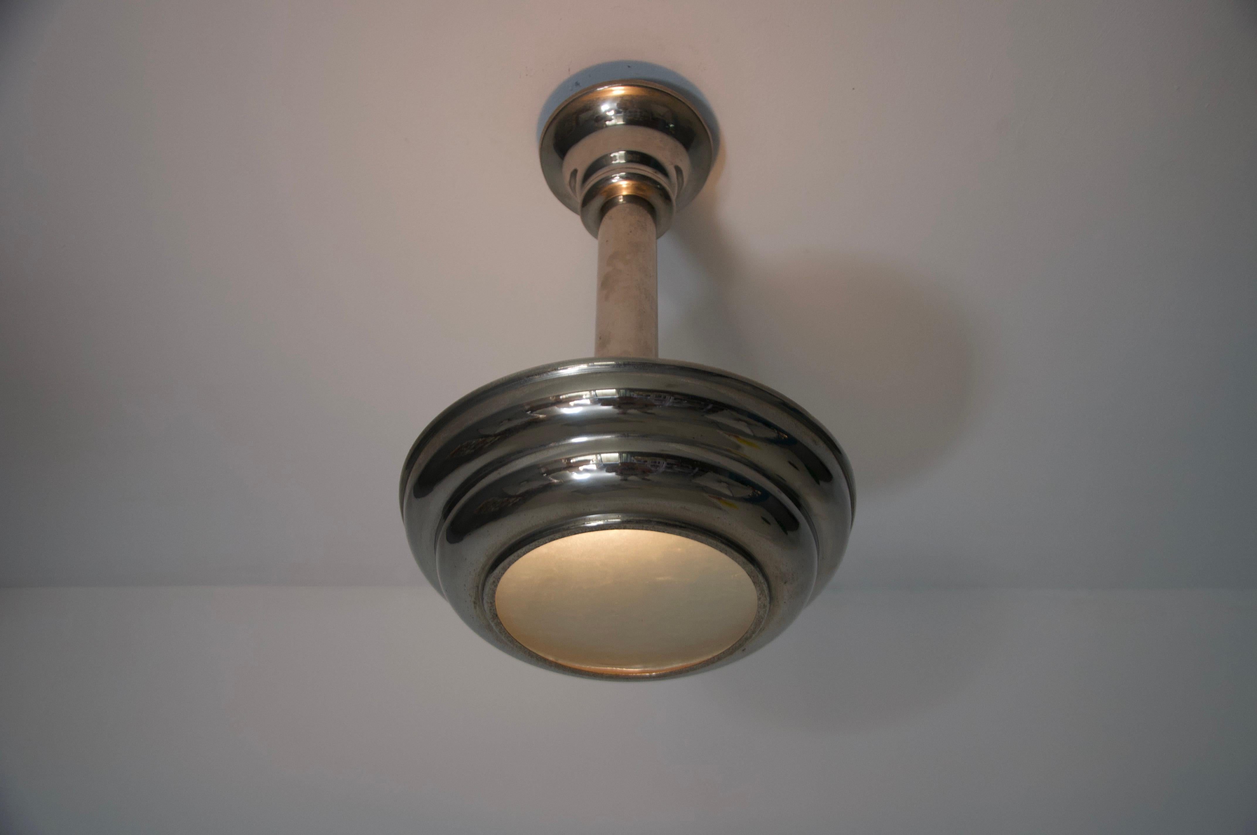 Questa autentica lampada da soffitto Art Deco della Germania degli anni '30 presenta una raffinata combinazione di vetro smerigliato ed elementi cromati. Il paralume in vetro a gradini riflette la chiarezza geometrica tipica del periodo, mentre gli