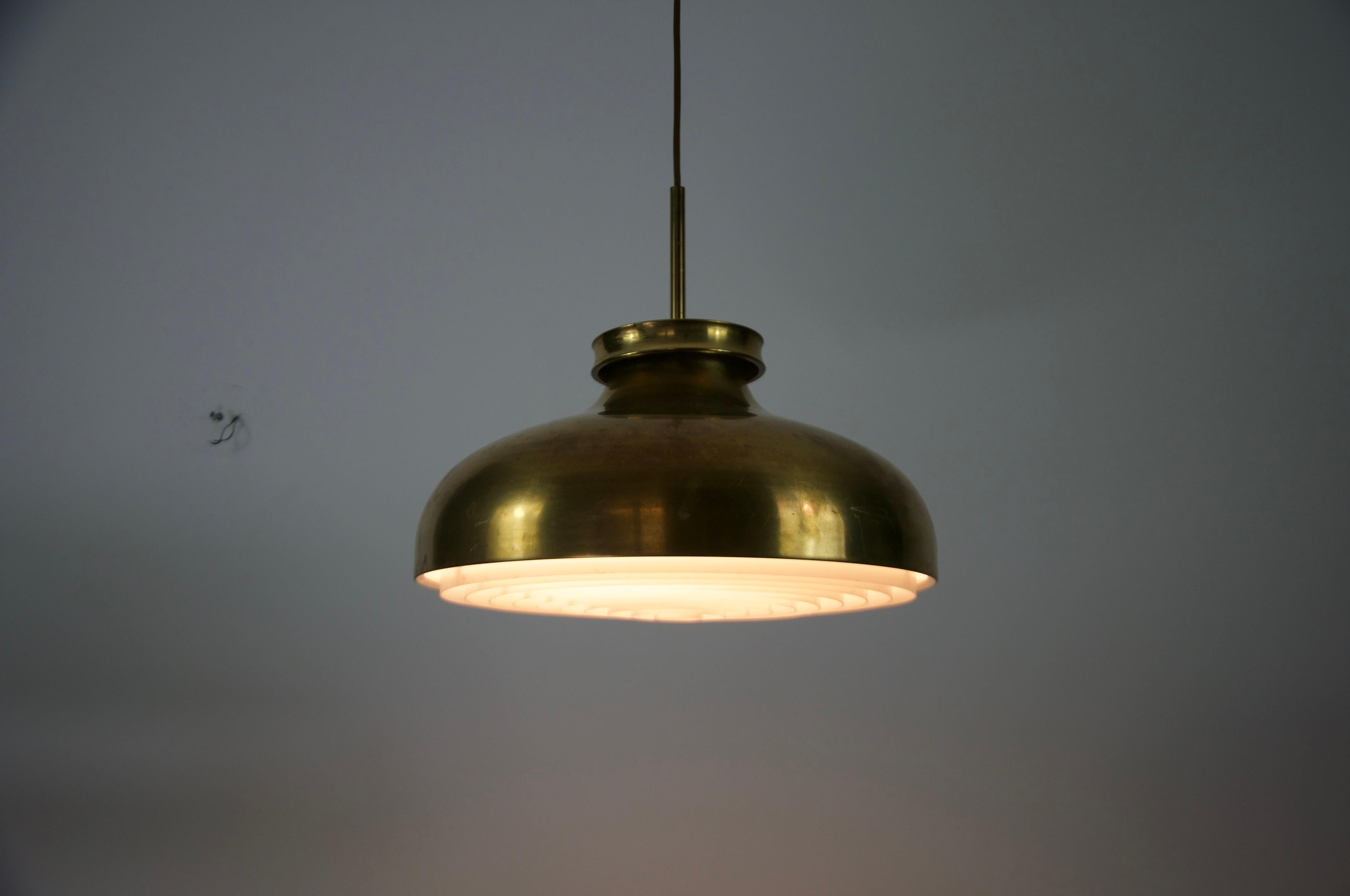 Questa elegante lampada a sospensione in ottone danese del Mid-Century degli anni '80 incarna il design scandinavo senza tempo grazie alla sua forma minimalista e ai materiali di alta qualità. La lampada presenta un bellissimo paralume in ottone