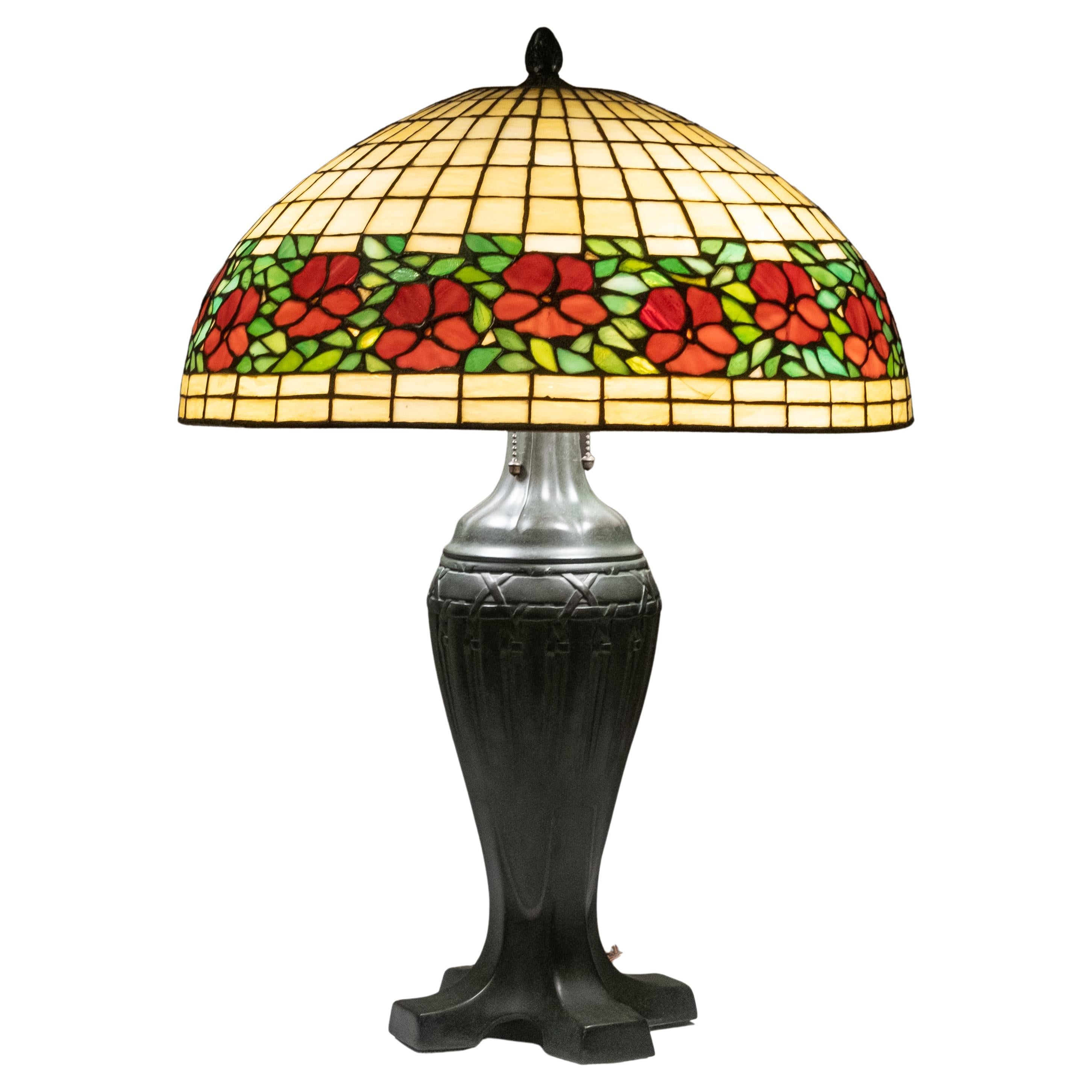Handel lamp Company. First quarter 20th century. Leaded stained glass 'Cherry Blossom' shade, on a Handel arts and crafts bronze urn-form base with three lights and acorn pulls. Marked to rim of shade 'Handel' flanked by stars;. The base is