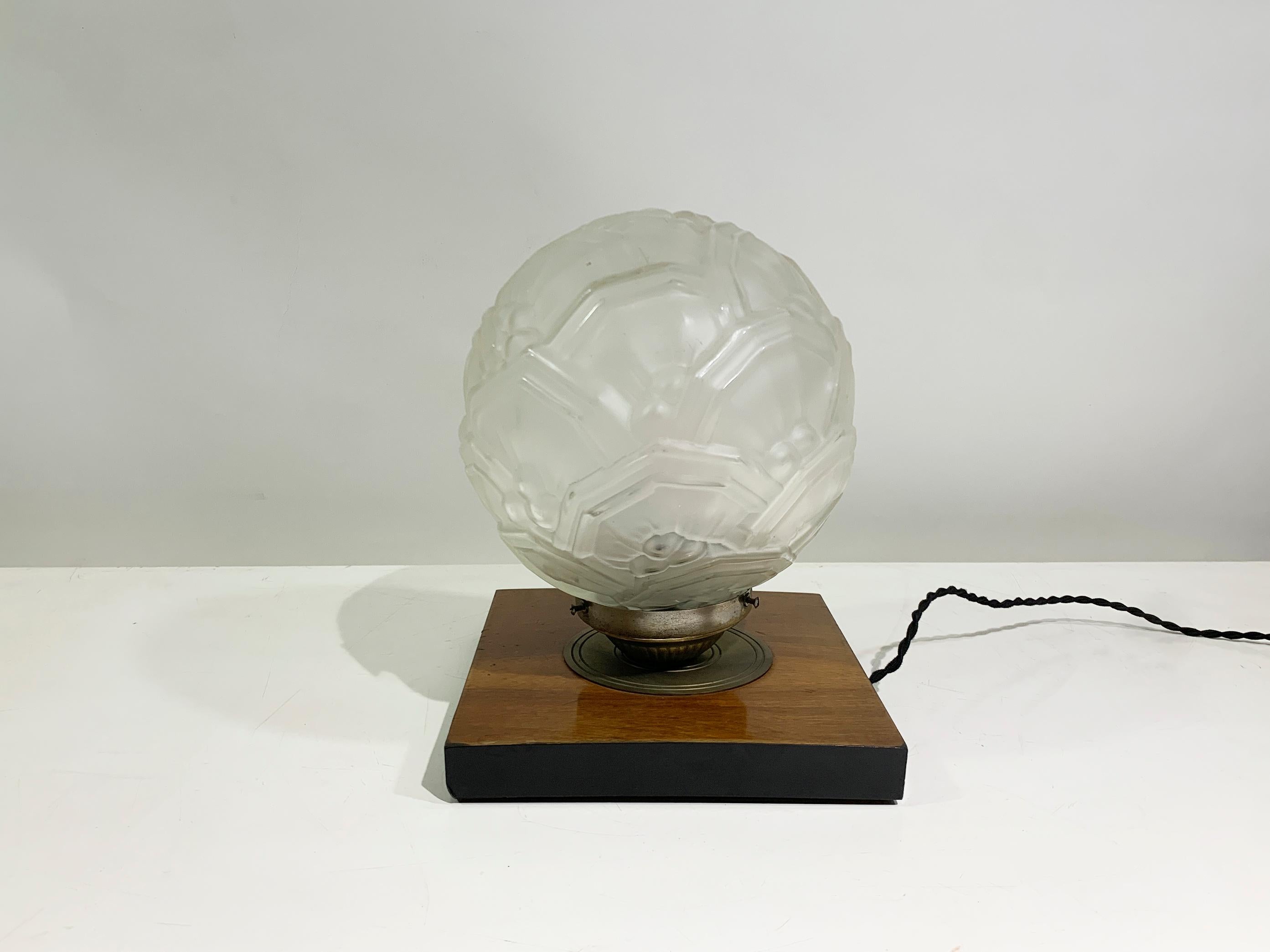 This exquisite Art Deco table lamp, dating from the 1930s, embodies the sophisticated elegance characteristic of the era. The table lamp features a striking spherical shade crafted from frosted glass, intricately molded with geometric patterns and
