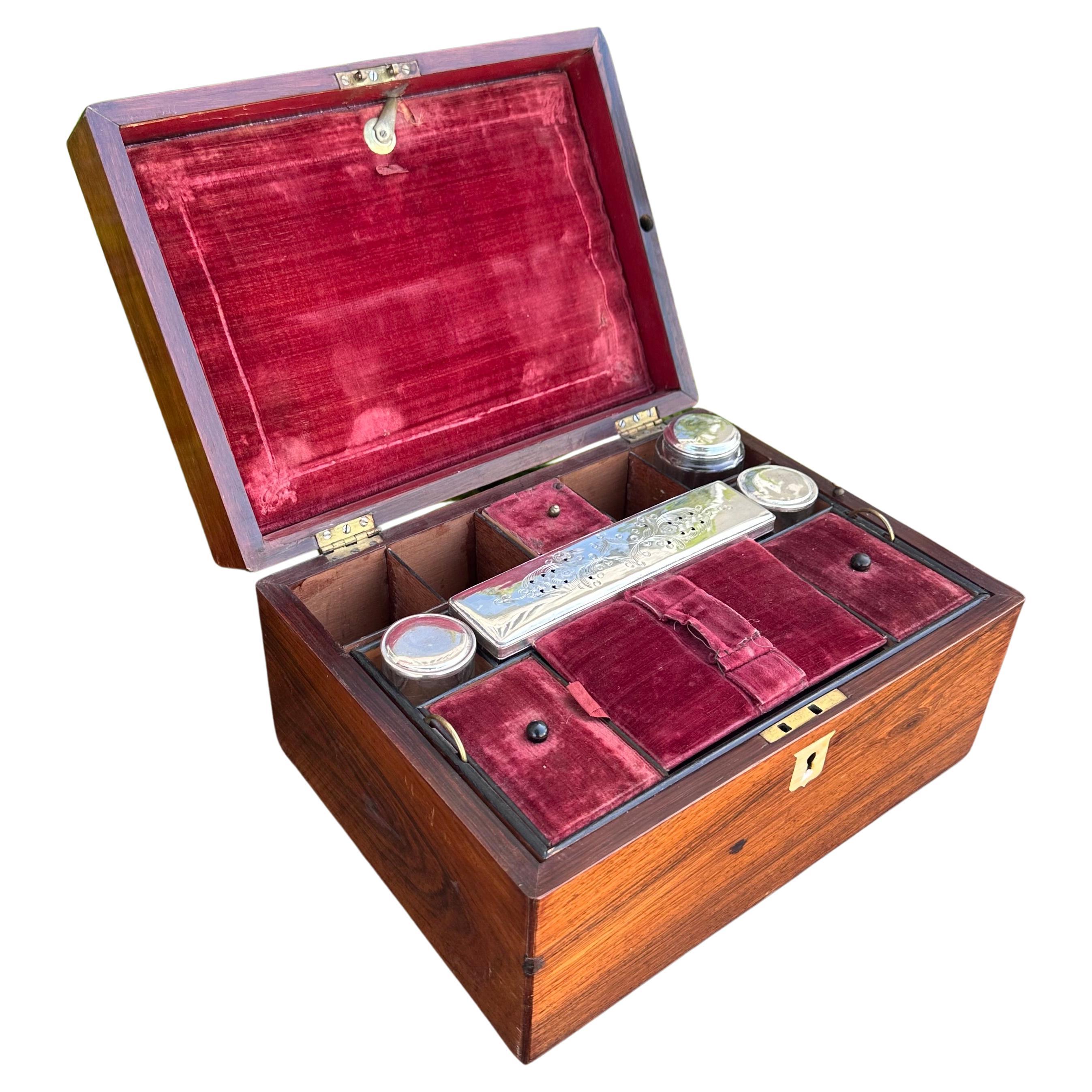 Antiguo tocador o caja de viaje de caballero de nogal. Incluye un interior de terciopelo rojo y frascos y caja originales de cristal y chapados en plata con un compartimento secreto accionado por resorte que se abre con una palanca.