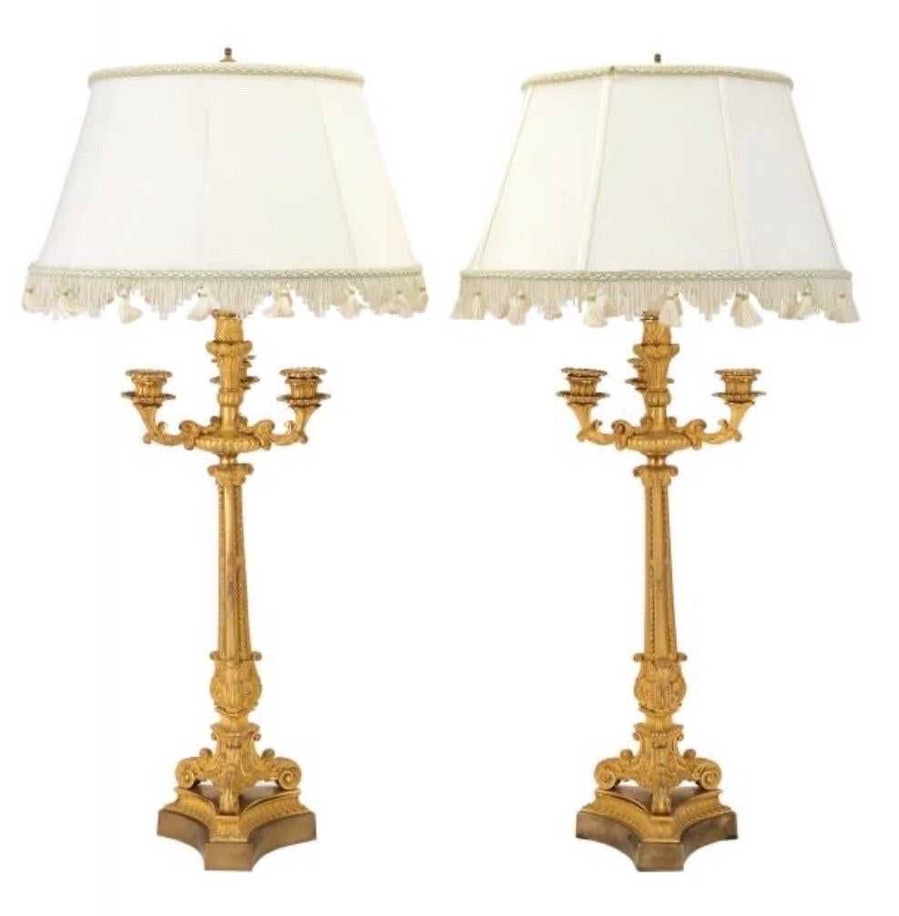 Pair of 19th century French ormolu four-light candelabras now electrified into lamps. Each with flaring triangular stem surmounted by a nozzle centering three scrolling candle arms, the scrolling feet on a triangular plinth.