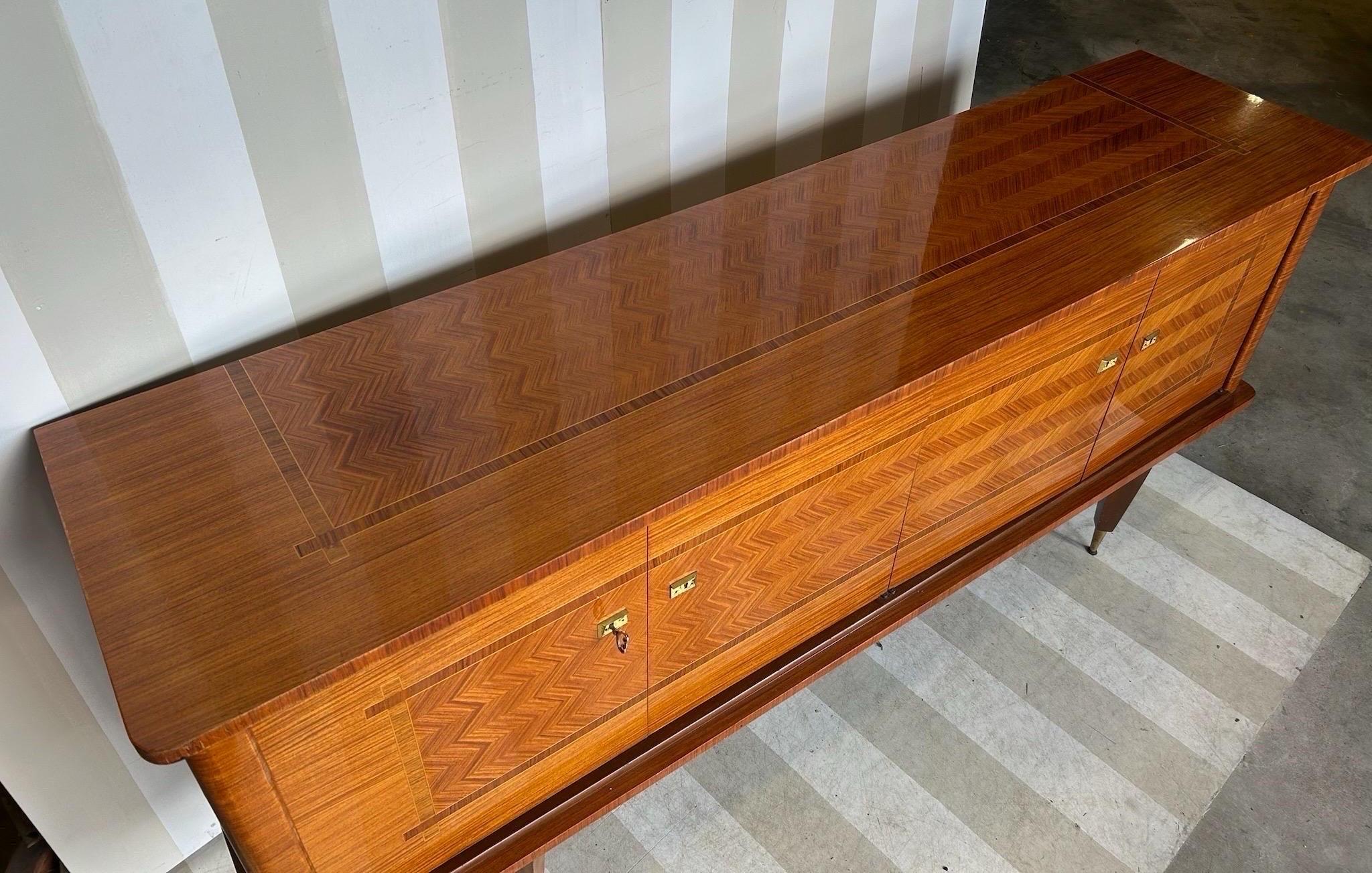 Splendida credenza francese della metà del secolo scorso con interni attrezzati. Questo pezzo è caratterizzato da un intarsio in noce a motivo di parquet o chevron con bordatura trasversale in macassar, ferramenta originale e piedini in ottone.