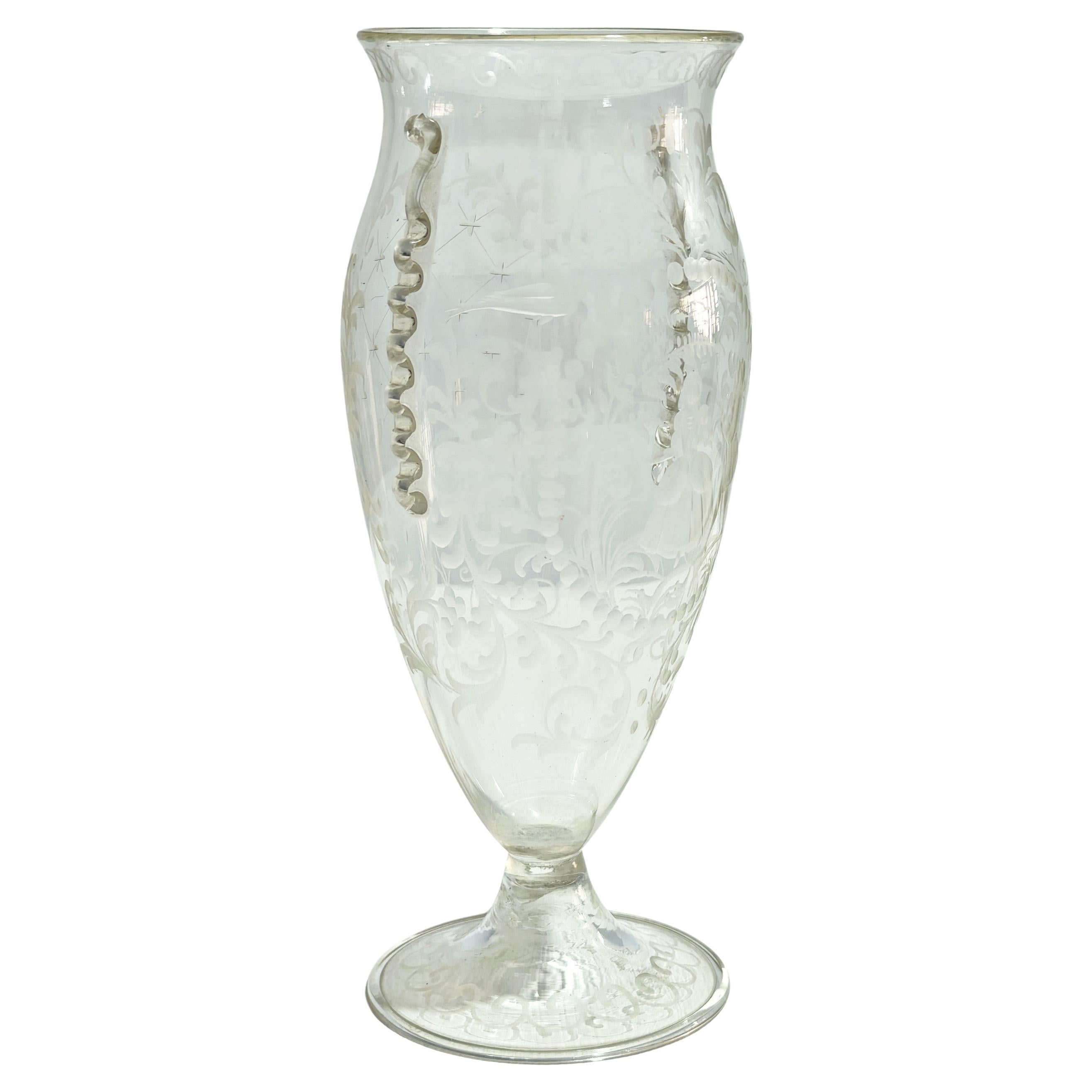 GUIDO BALSAMO STELLA Produzione S.A.L.I.R., Italia 1920/30. Vaso a goccia in vetro soffiato incolore con bocca leggermente svasata su un piede in vetro soffiato con manici applicati, decorazione di figure con scena galante incisa e motivi vegetali.