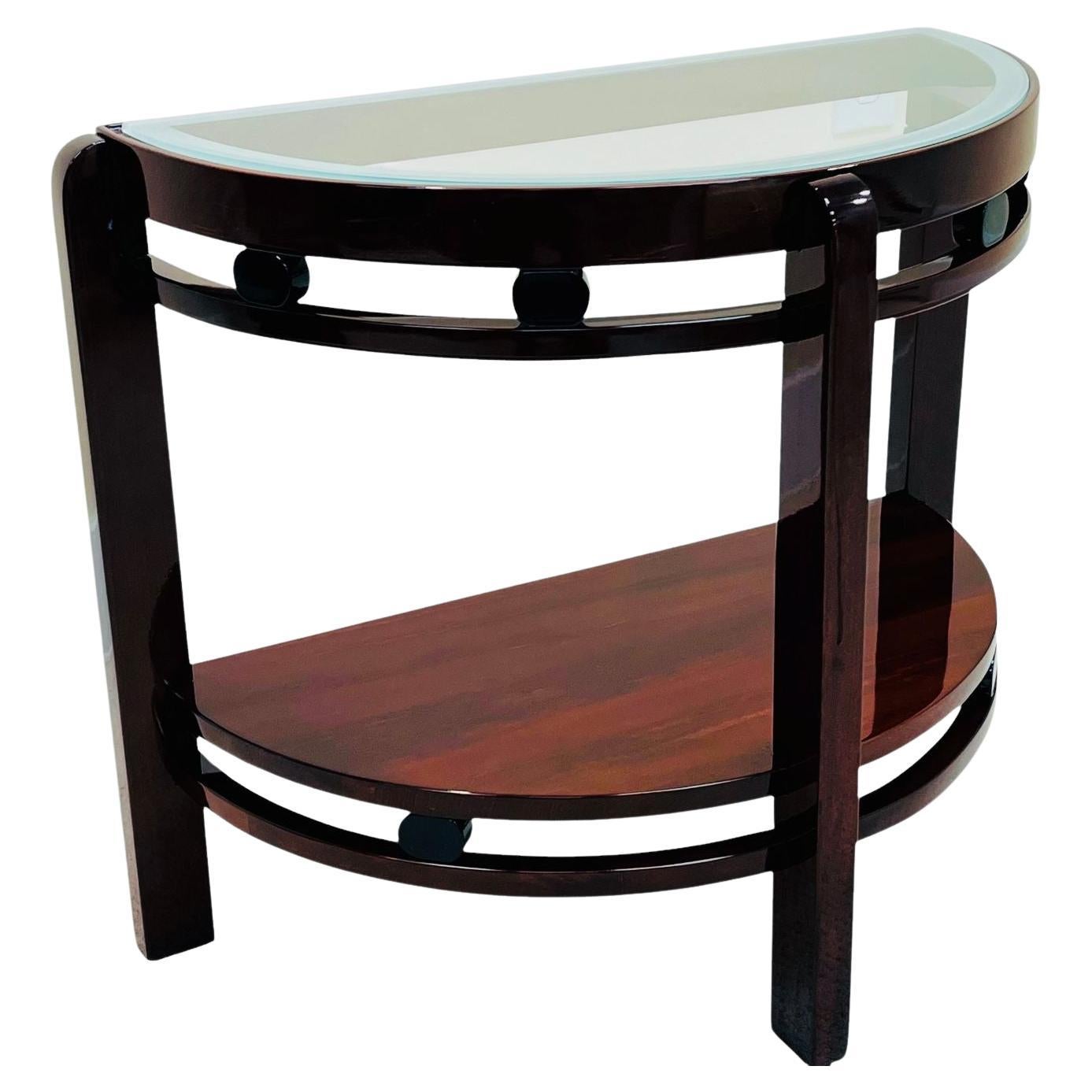     Superbe table d'appoint Art Déco en demi-cercle, datant des années 1930. Fabriqué de manière experte en acajou teinté érable avec des accents ovales laqués noirs et un plateau en verre aux bords joliment sablés. Un exemple élégant et