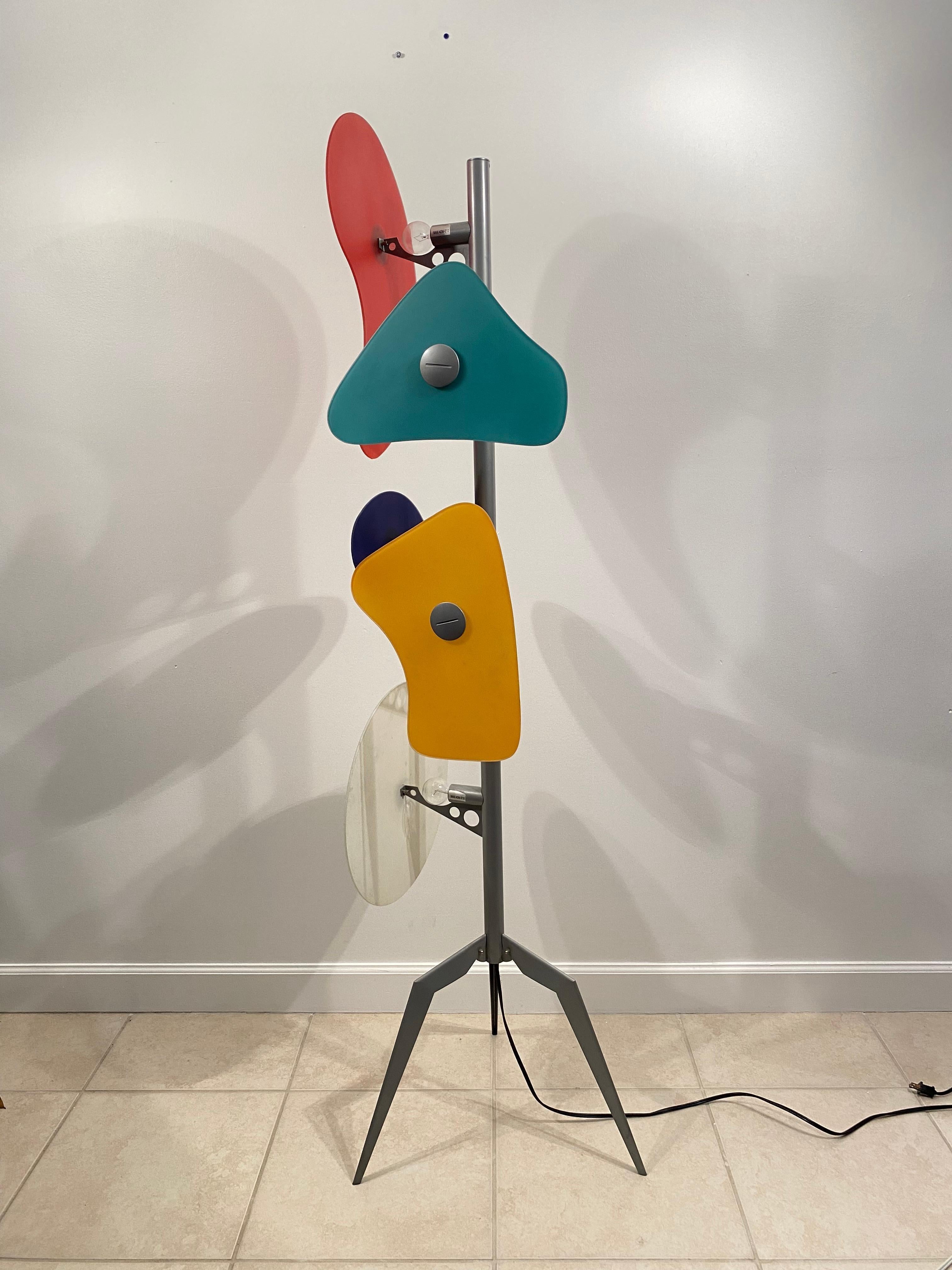 Orbital Floor Lamp consisting of 5 backlit multi-color glass shapes with large screws attached to a gray lacquered metal base.  The Orbital Floor Lamp was designed in 1992 by Ferruccio Laviani and manufactured by Foscarini.