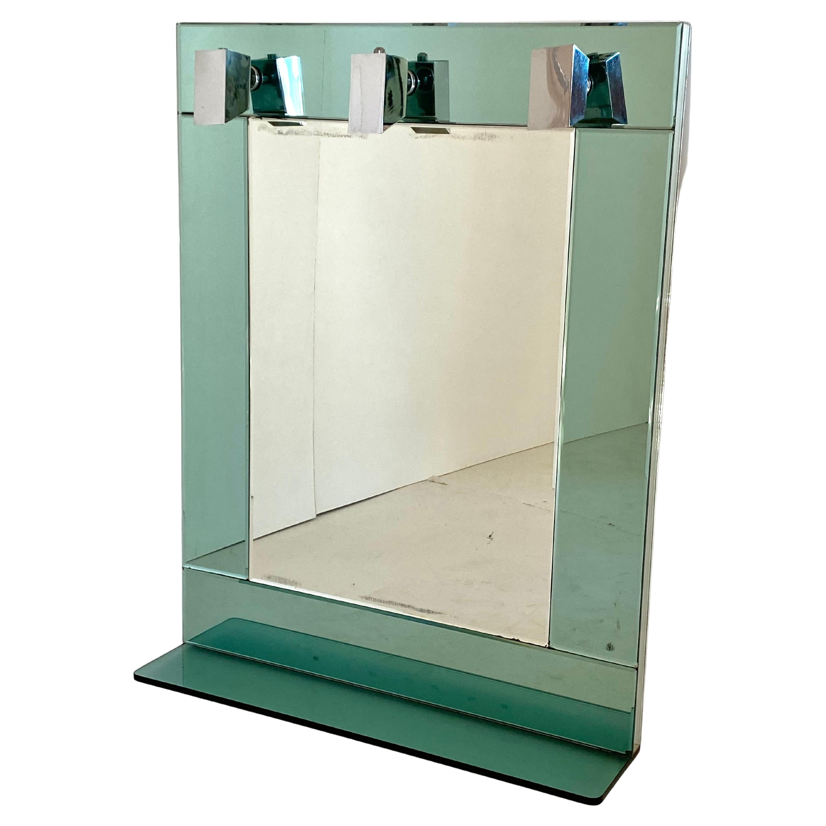 A 1970s vintage wall mirror with three lights spots. Manufactured in Italy, the glass is made by aqua glass mirror and chromed lights spots. The lower glass shelf can be easily removed if needed. Electrical parts have been revised by a professional