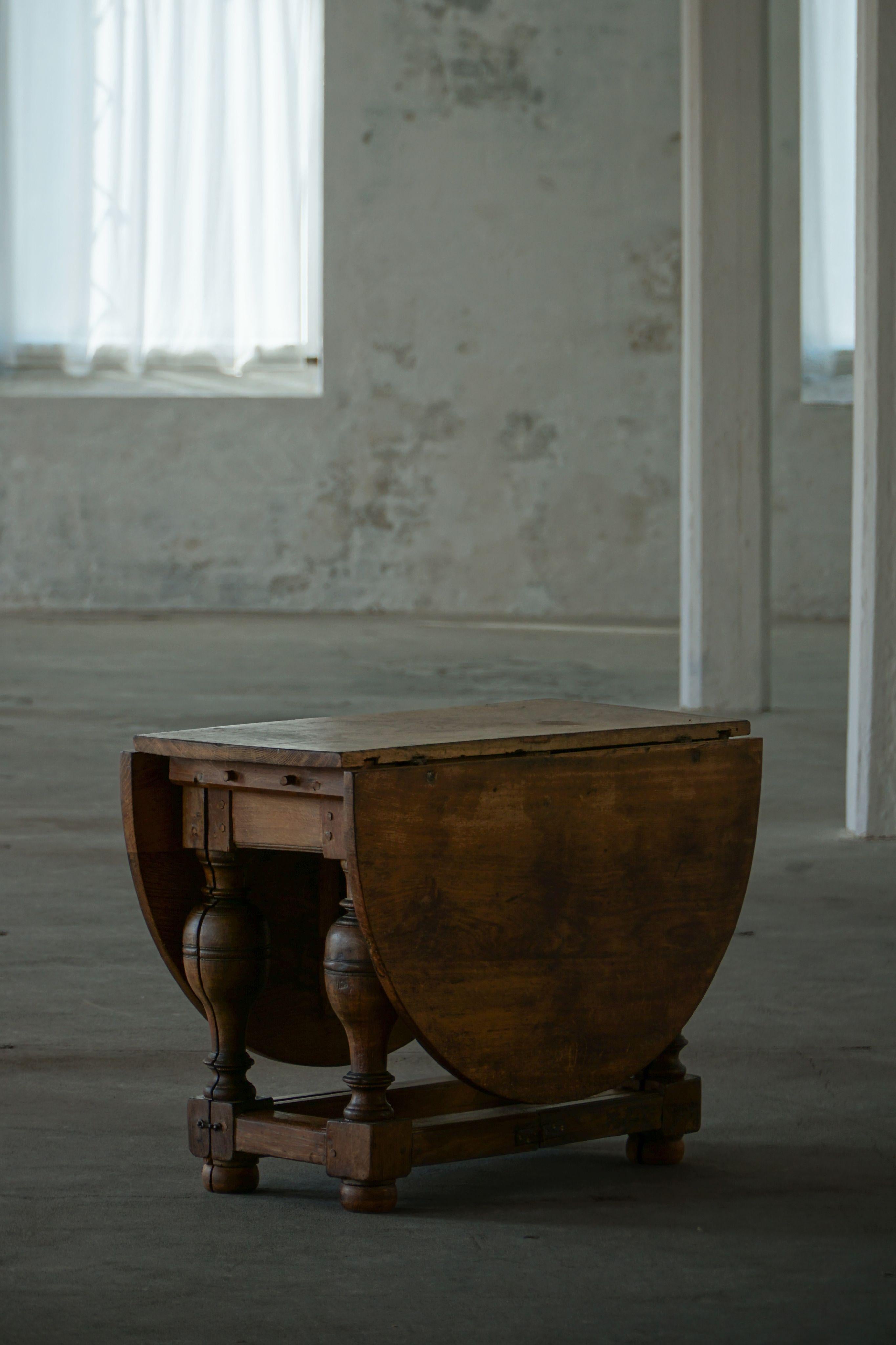 This antique Baroque drop-leaf table, crafted by a skilled Danish cabinetmaker in the 19th century, radiates timeless character and quiet elegance. Made from solid oak with a rich patina, the table features beautifully turned legs and a robust