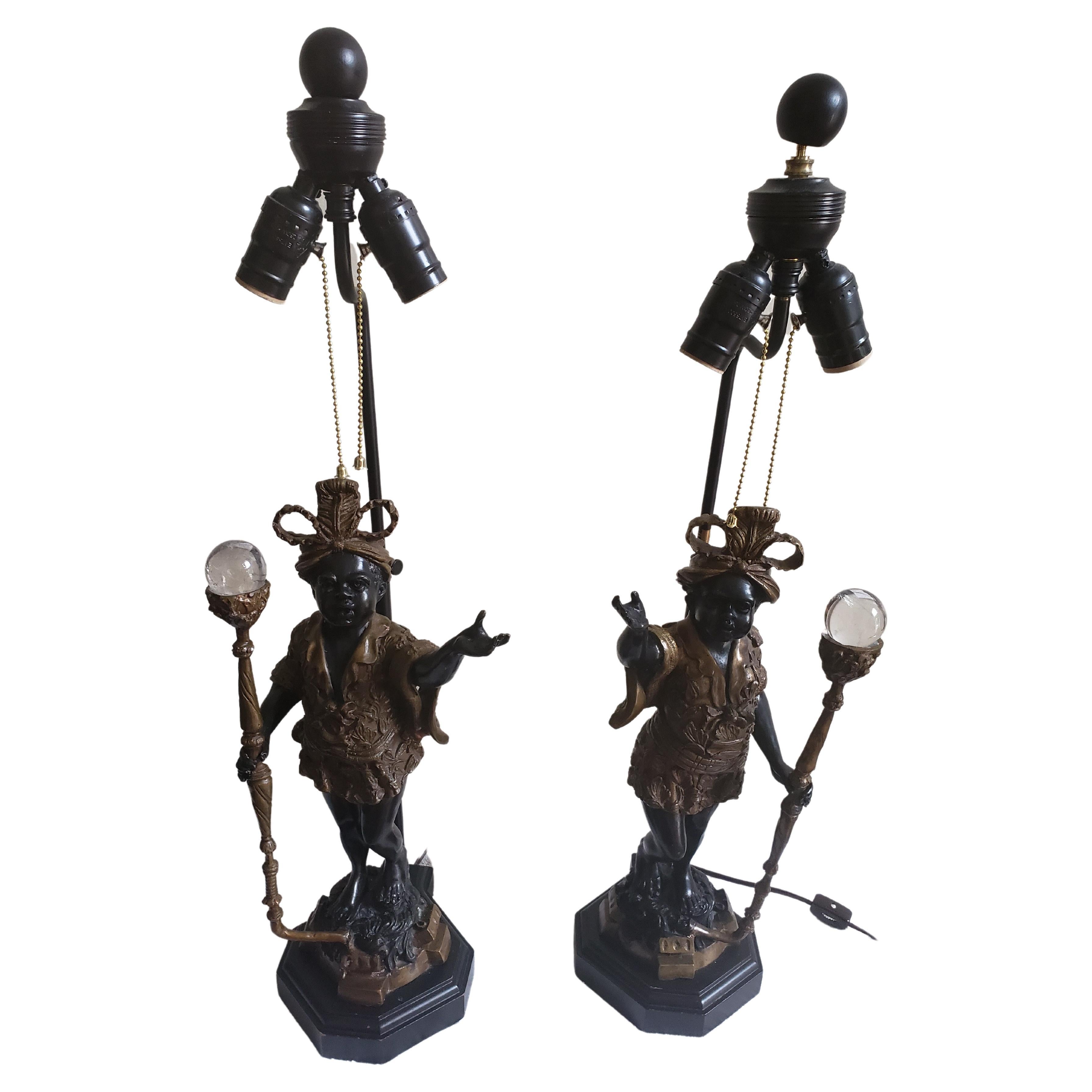 Paire de lampes antiques vénitiennes. Cette paire de garçons figuratifs avec leurs torches d'éclairage est coulée en bronze avec les traditionnels vêtements clairs et dorés sur fond noir. Elles sont montées sur un socle en bronze foncé. Les deux