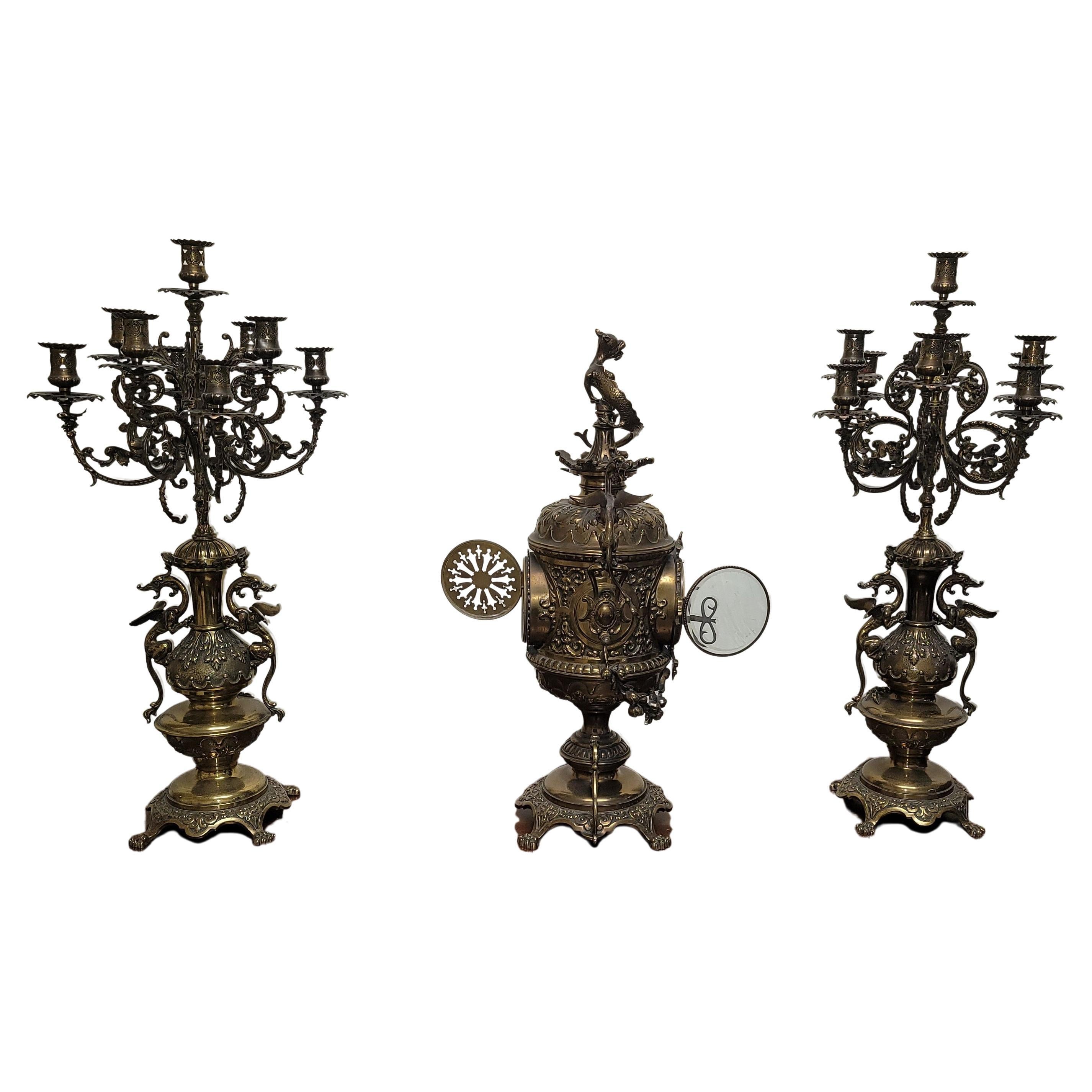 Ensemble de trois chandeliers et d'une horloge en métal doré de style Empire belge Belle Epoque, d'inspiration asiatique. 
Ils mesurent 11