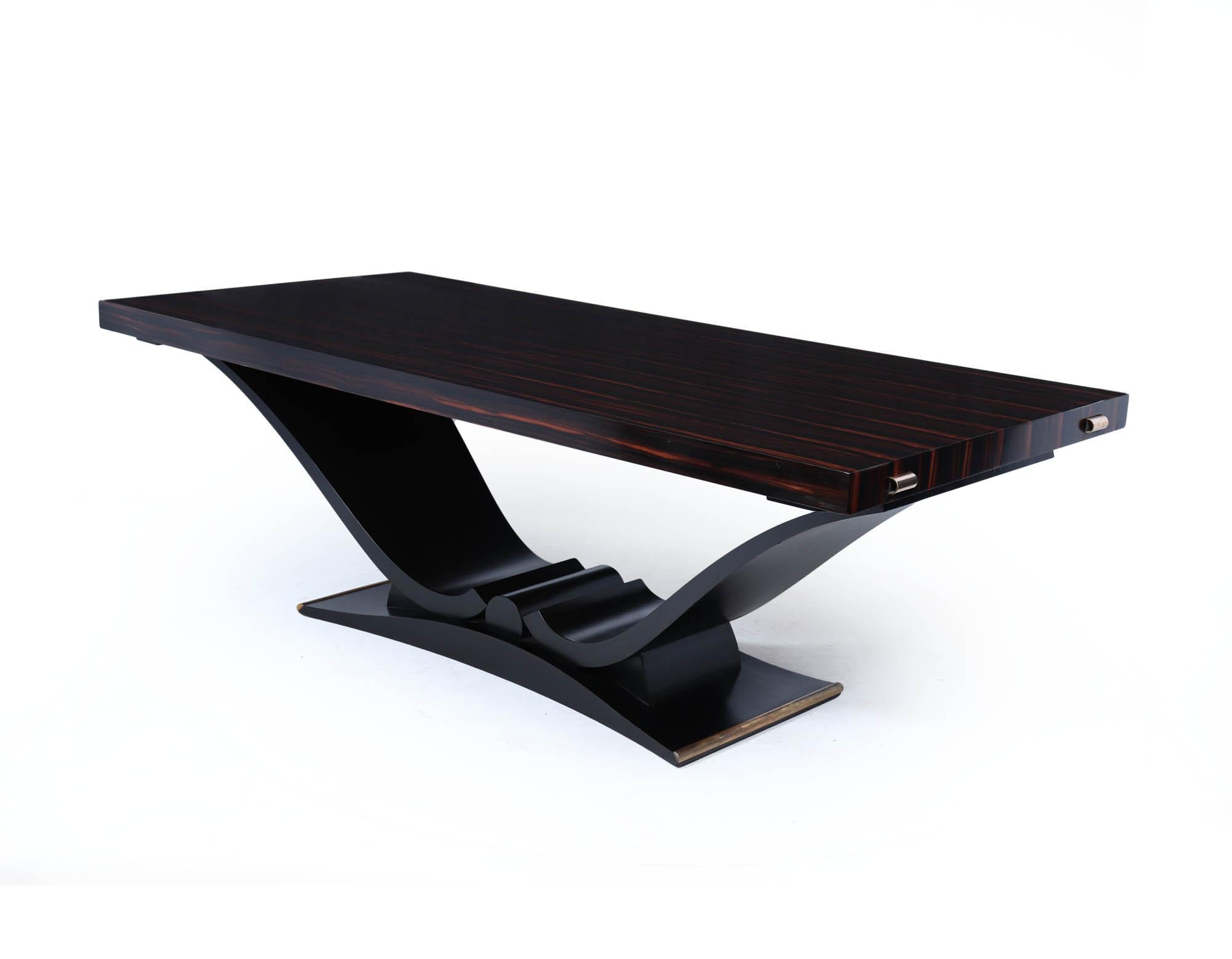 A dramatic and finely crafted French Art Deco dining table in richly figured Macassar ebony. The rectangular top sits over a sculptural black lacquered base with sweeping curves and scalloped details. At each end of the table are discreet brass