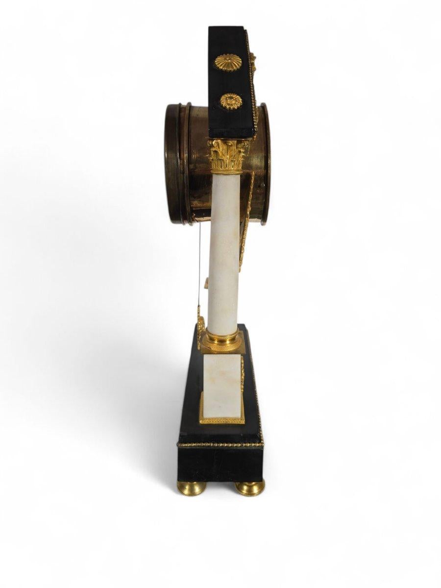 Refined French Empire-style portico clock, dating from the early 1800s, in black and white marble, richly adorned with finely chiseled gilt bronze. The enameled dial with Roman numerals is signed, set within a pediment-like architectural structure
