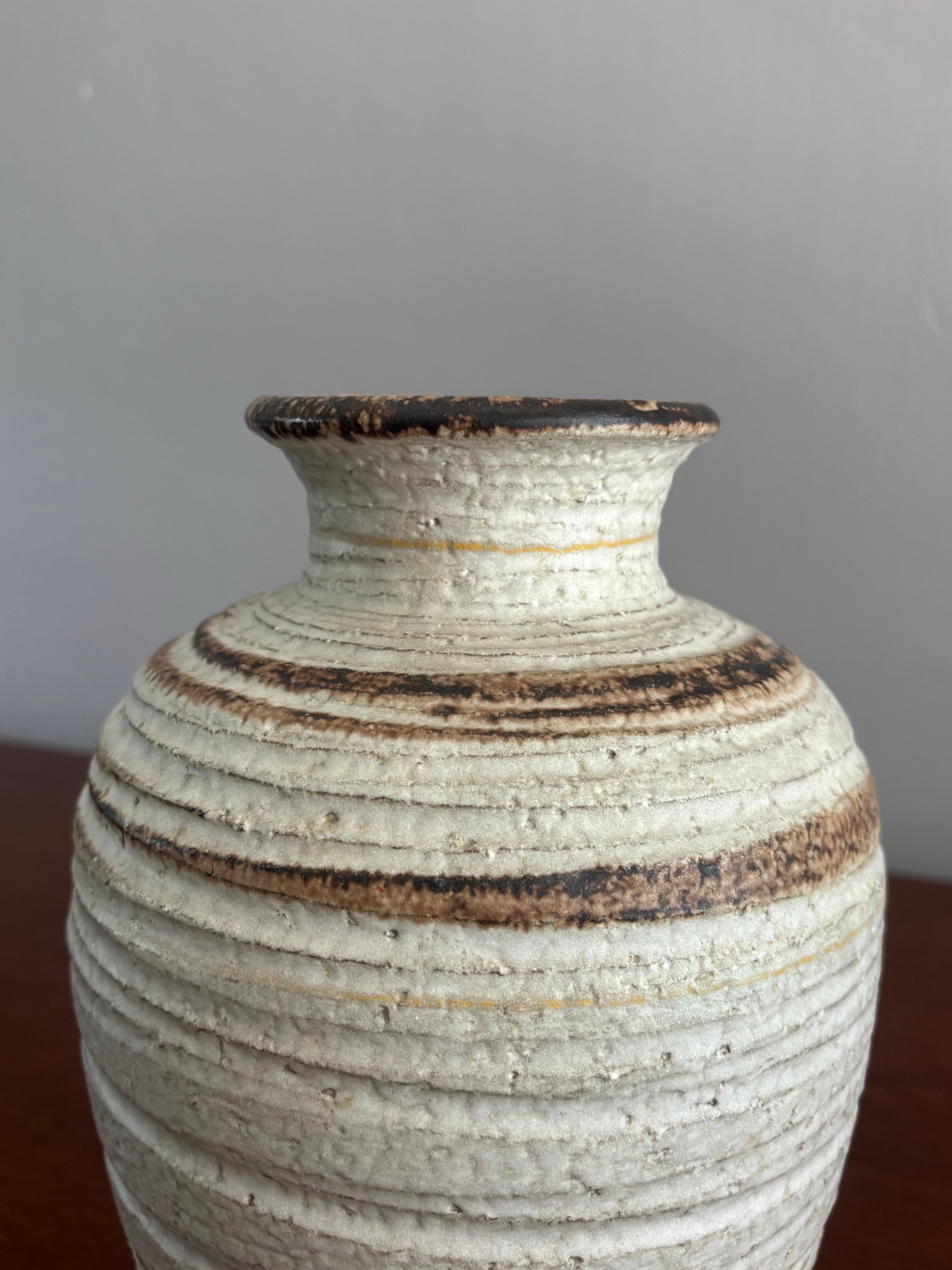 A large scale hand thrown vase. Made by Bitossi for Rosenthal Netter. A beautiful rotation of creamy neutral and brown tones. Rotating line details give the piece an organic movement when looking at it. 

Signed on the bottom. 

Vase is 10” tall and