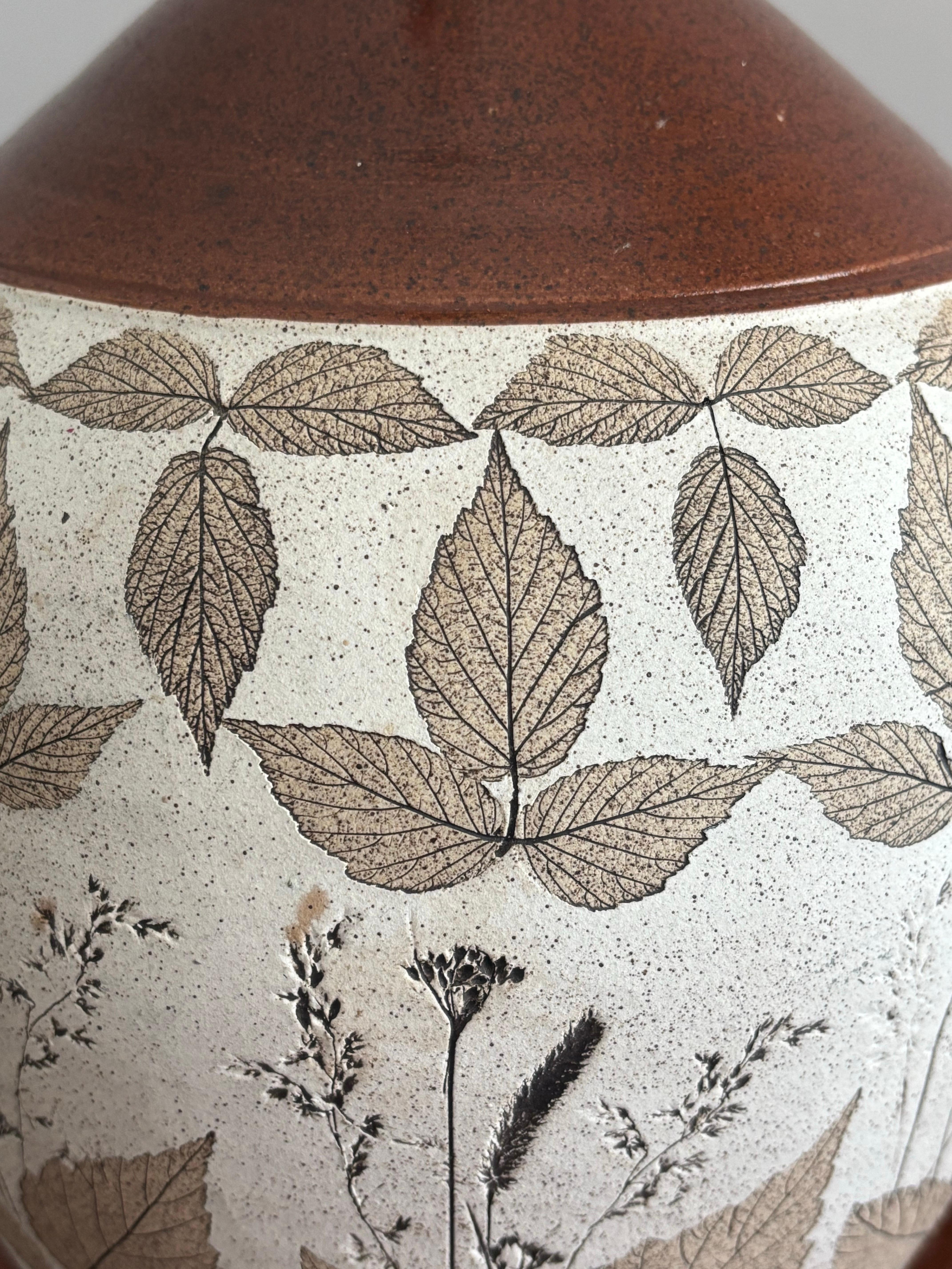 Lámpara vintage de cerámica de barro en excelente estado. Hermosos colores terrosos de tostado y un rico marrón esmaltado en la parte superior. Decorada con hojas impresas que forman un dibujo bello y natural. 

La lámpara mide 18,5