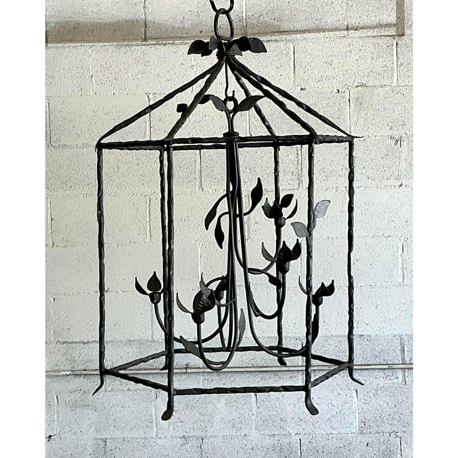 Discover the dramatic elegance of this vintage candle lantern, a substantial and sculptural piece crafted from hand-forged metal. Its impressive design features an open, multi-faceted frame adorned with intricate vine and leaf motifs, creating a