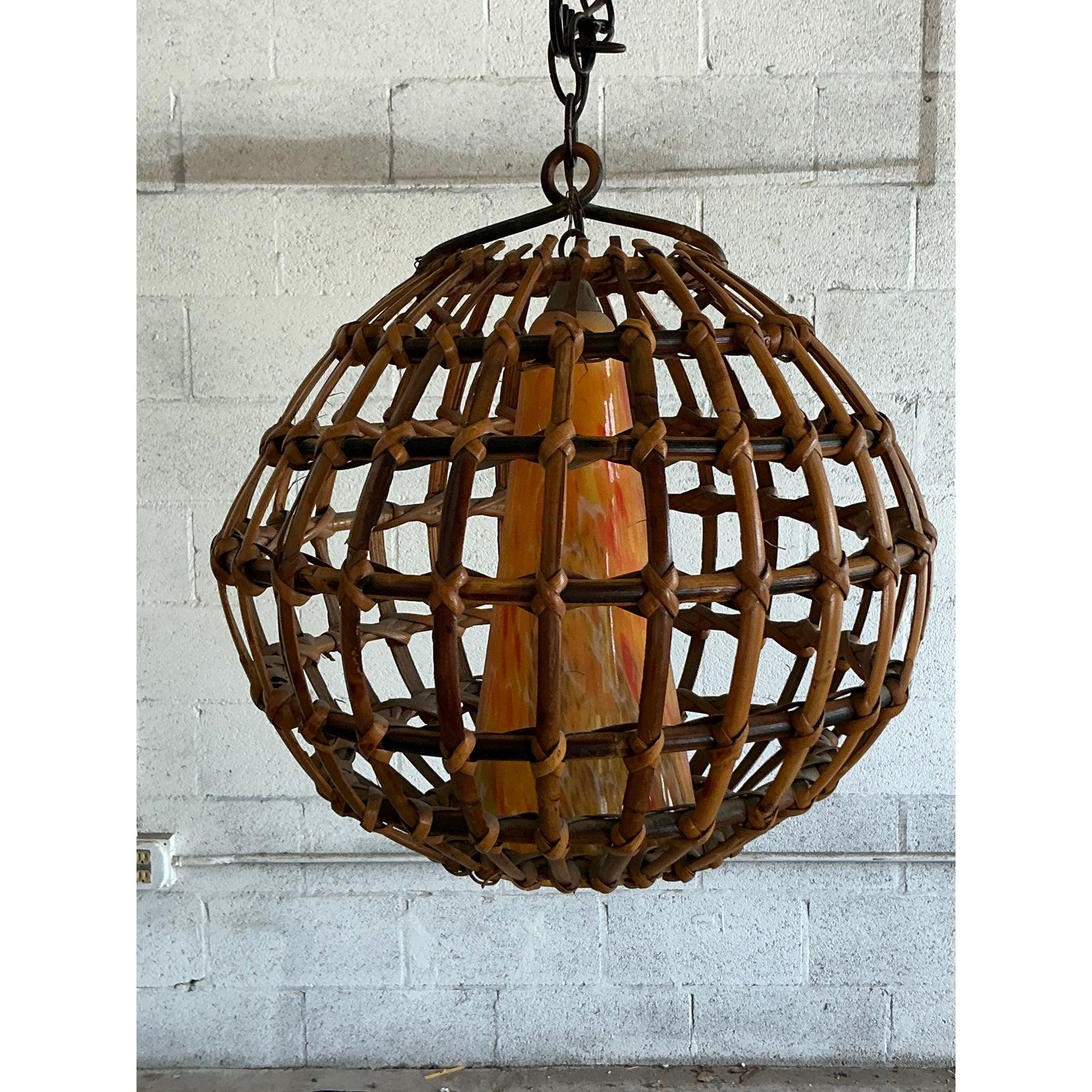 Abbraccia la bellezza organica della natura con questo accattivante lampadario vintage, una miscela armoniosa di rattan intrecciato a mano e vetro soffiato artigianalmente. Questo apparecchio unico è caratterizzato da un'impressionante gabbia