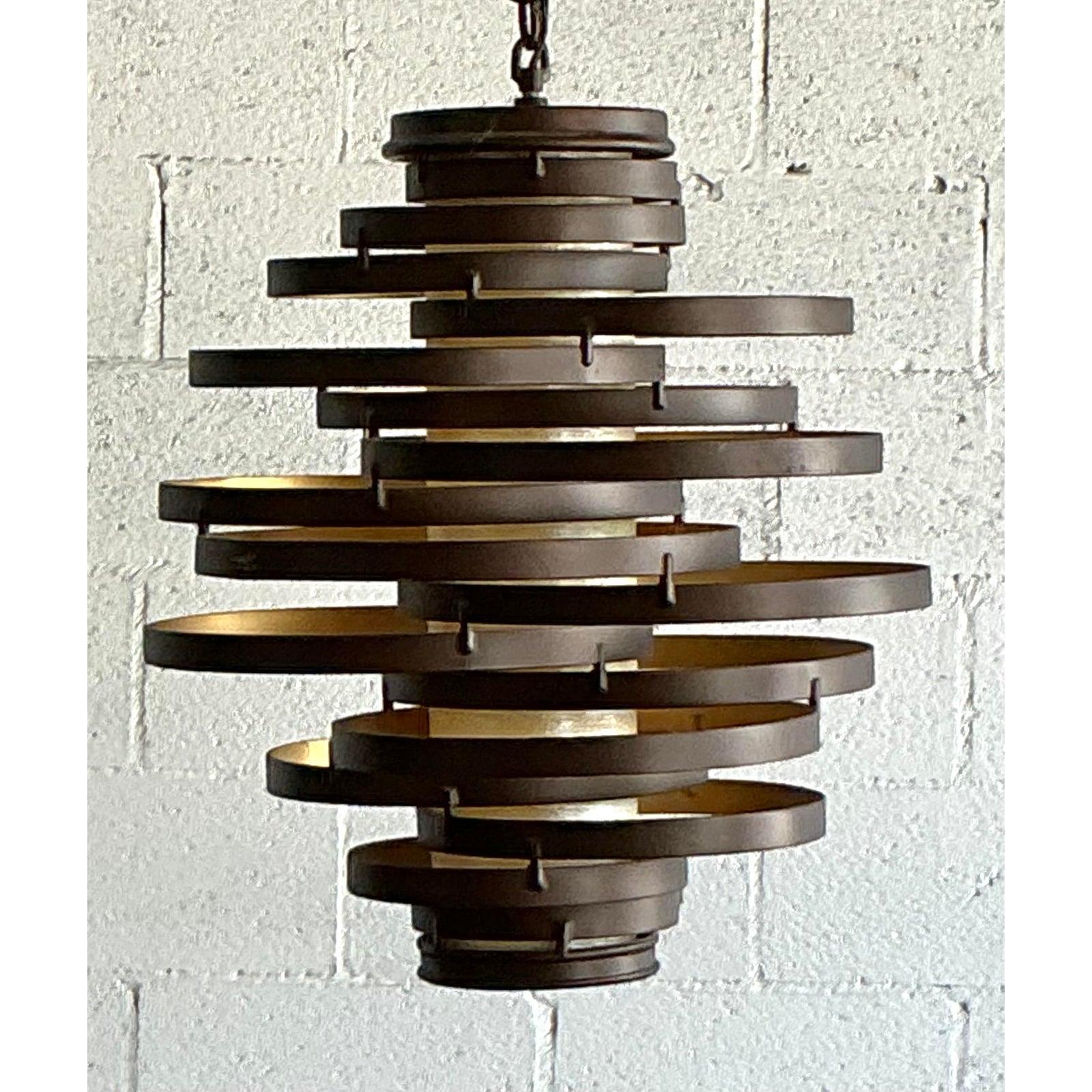 Crea un'audace dichiarazione architettonica con questo iconico lampadario a spirale vintage. Esempio magistrale di design scultoreo del Mid-Century Modern, questo pendente è caratterizzato da un vortice dinamico e a cascata di fasce di metallo scuro