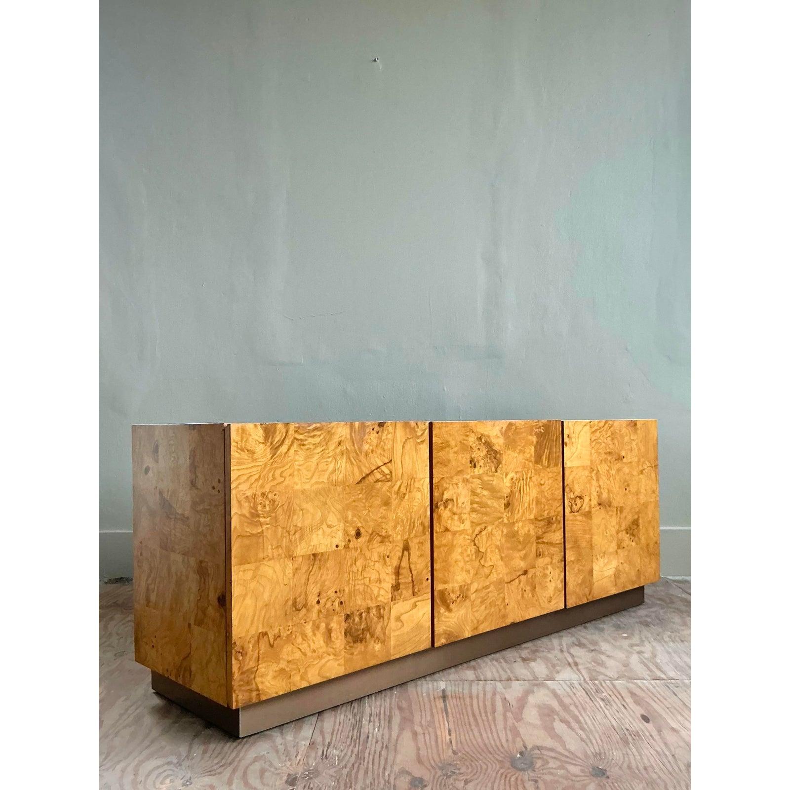A stunning homage to the iconic work of Milo Baughman for Thayer Coggin, this vintage credenza is a masterclass in minimalist design and material reverence. The cabinet is wrapped in a breathtaking expanse of bookmatched burl wood, whose swirling,