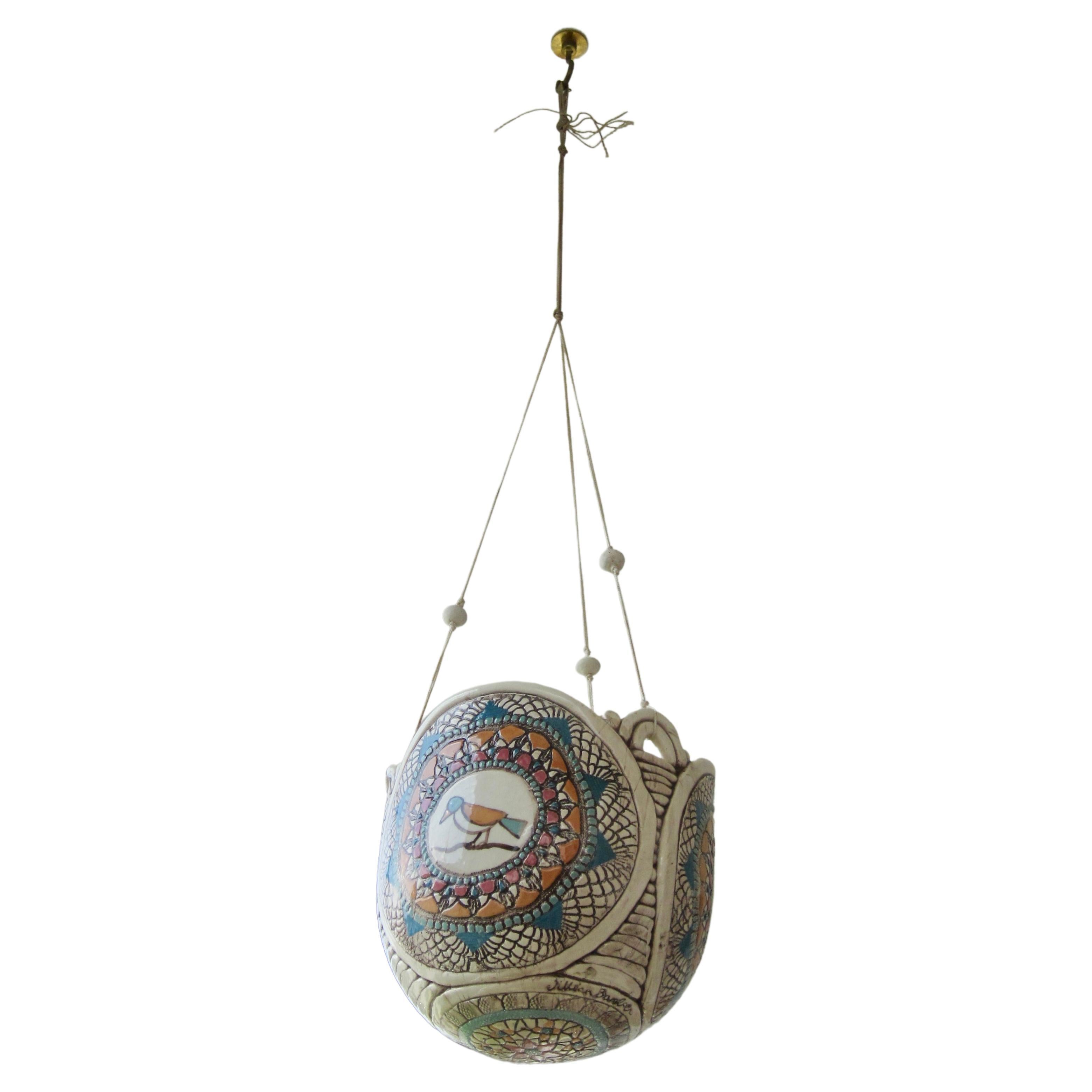 A textural three sided planter pot featuring a bird on each side and floral design on underside. The sculpture will not rest flat on a surface as it is meant to be hung. The nylon threading used for hanging is adorned with three clay beads. Signed