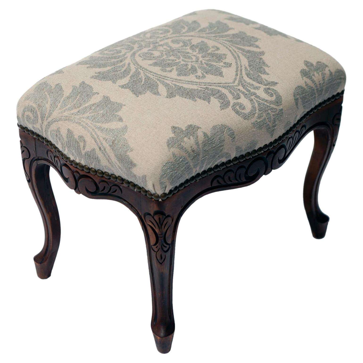Vintage French style Handcarved footstool upholstered in fine Italian linen wool blend. The stool is finished with antiqued brass nailheads.

