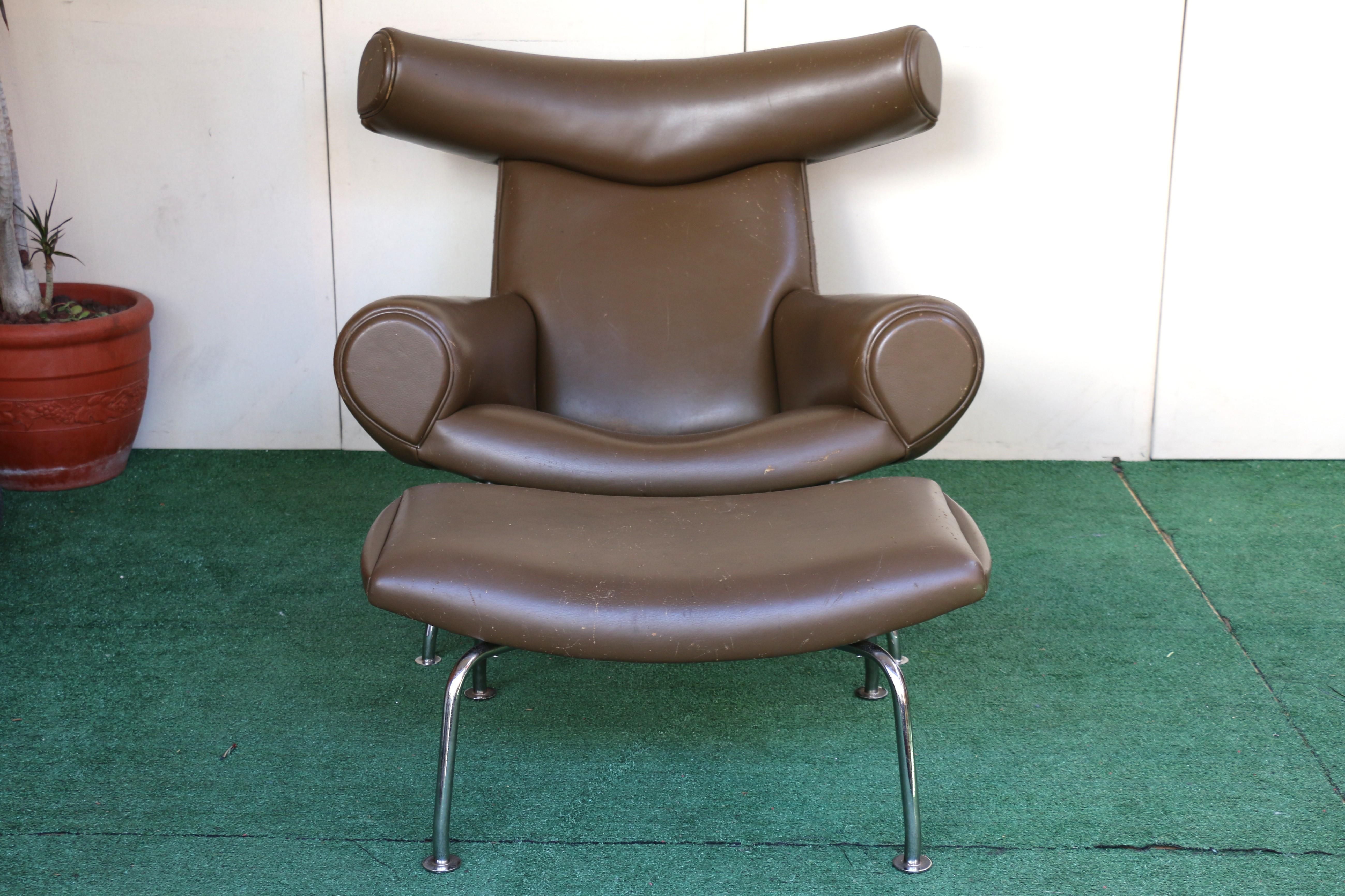Merveilleux fauteuil en cuir marron avec ottoman conçu par Hans J. Wegner, (il n'y a pas de marque de fabrique). Ce meuble emblématique, conçu en 1960, est connu pour sa forme sculpturale et son appui-tête 