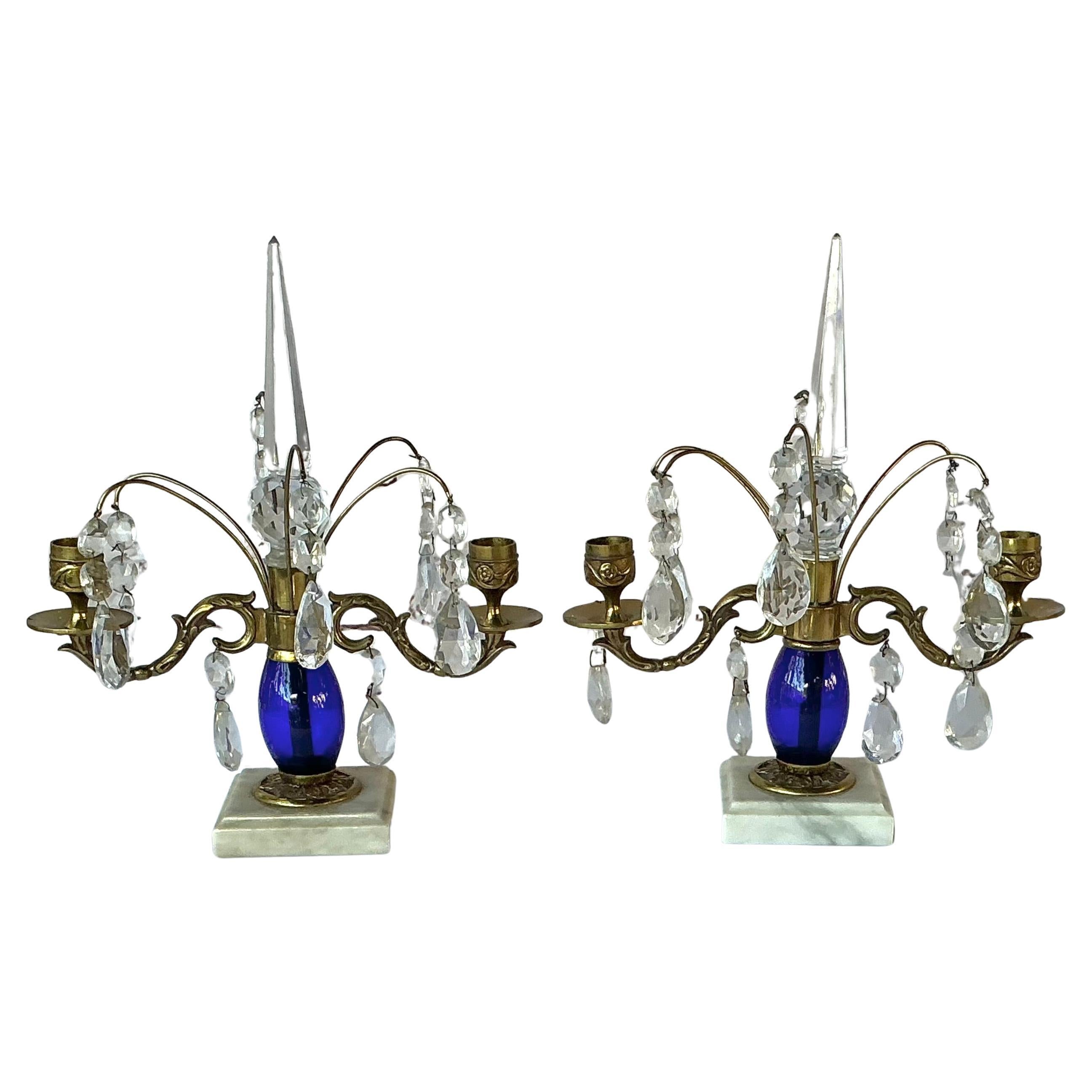 Coppia di eleganti girandole in stile gustaviano, XIX secolo. Fusti ovoidali blu cobalto appoggiati su una base di marmo bianco. Ognuno di essi ha due portacandele in ottone con delicati steli in ottone che reggono cristalli antichi pendenti e sono