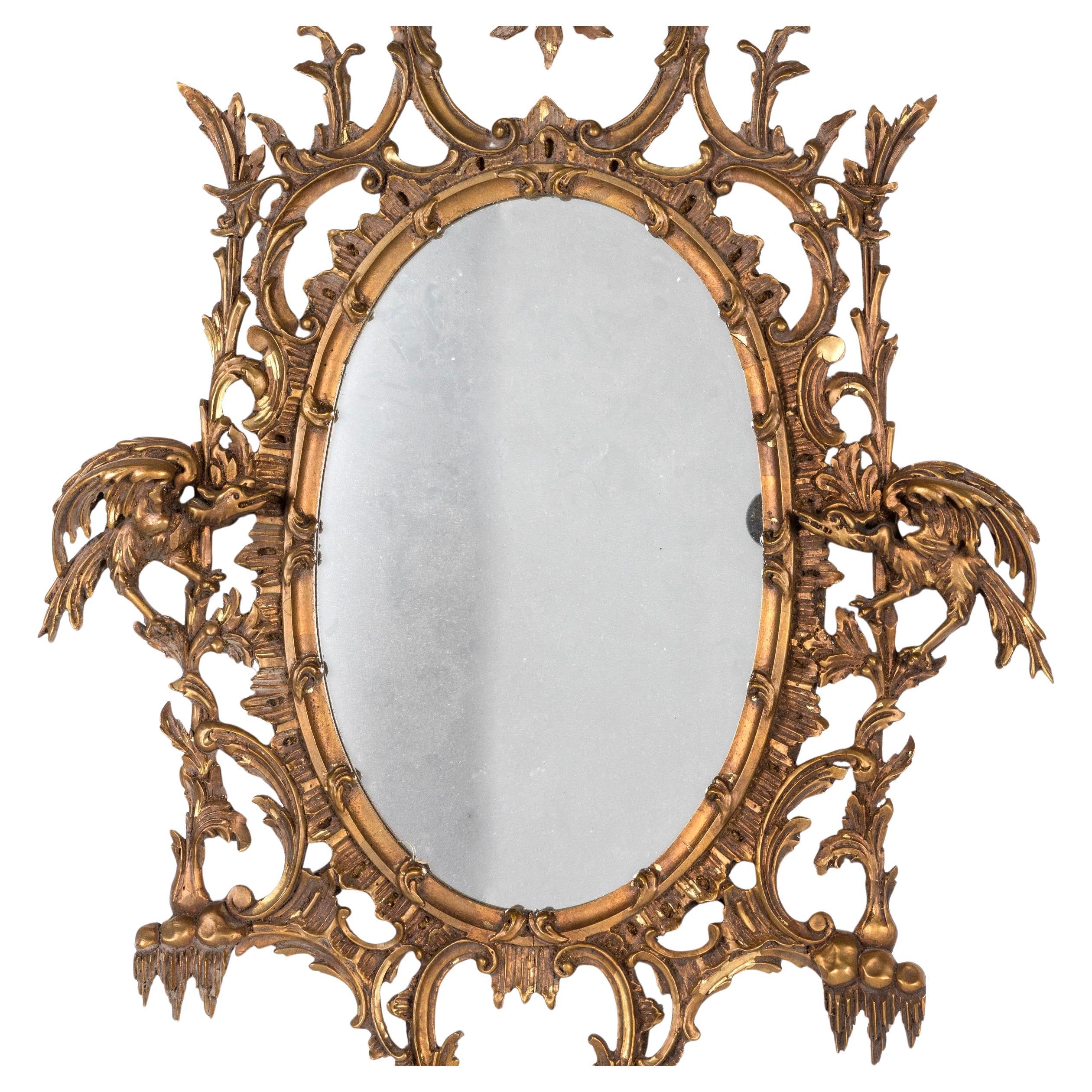 Miroir ovale de style Chippendale chinois du 20e siècle. Le miroir présente une plaque ovale encadrée d'une corniche en bois doré sculpté de façon complexe. Il est surmonté d'une crête sculptée de style pagode, ainsi que d'oiseaux phénix et de
