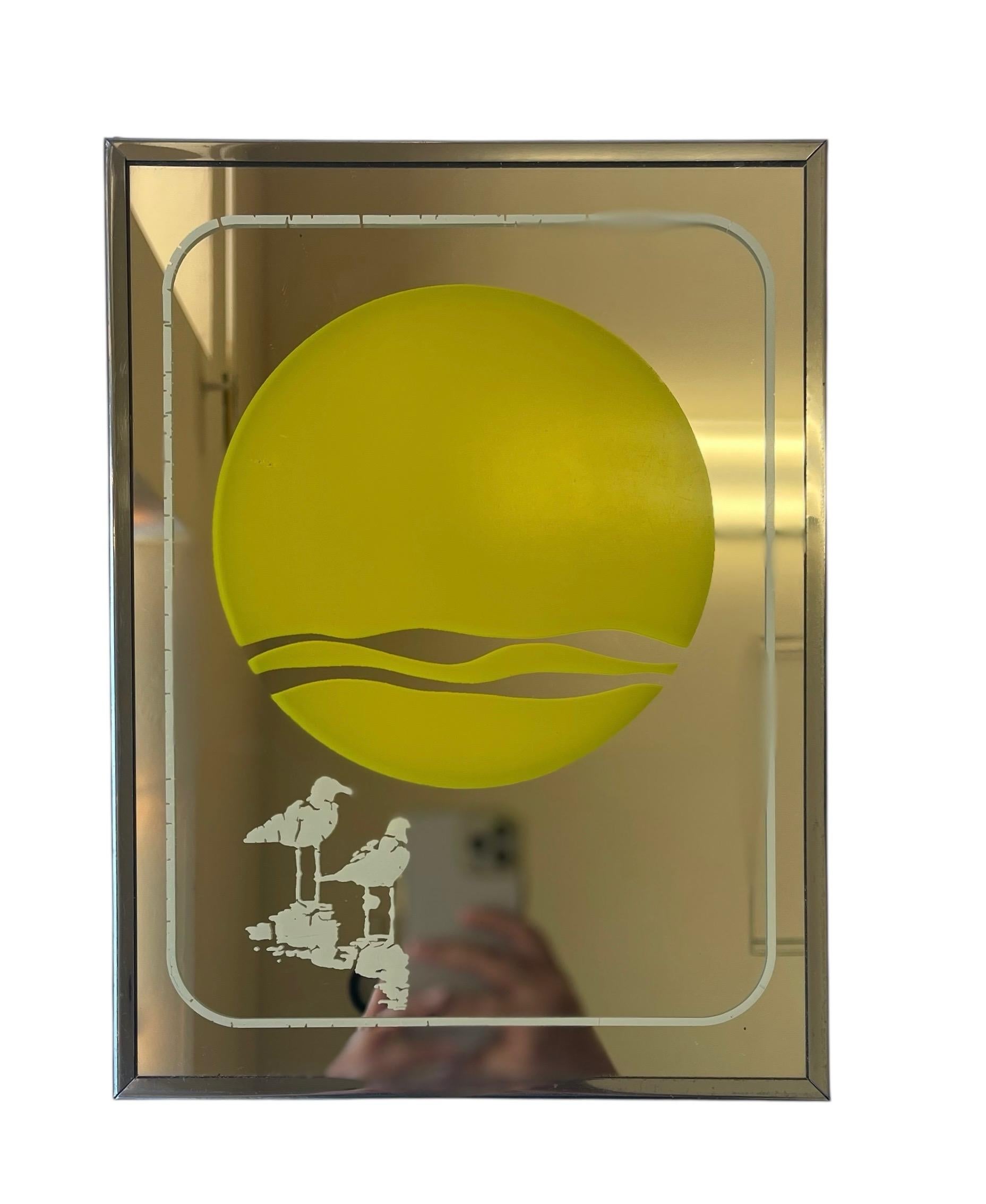 A striking 1970s decorative mirror manufactured by Mechanical Mirror Works, Inc. under their Brytone line, featuring a bold graphic depiction of a coastal sunset. The composition includes a large yellow sun with stylized cut-out wave lines, mirrored